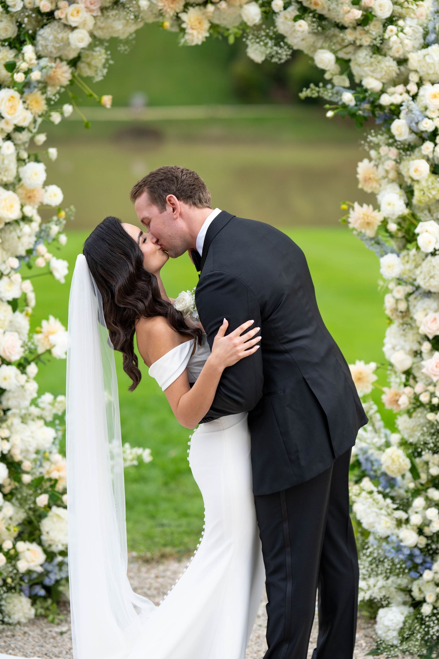Wedding ceremony setting with white floral arch and romantic garden backdrop.