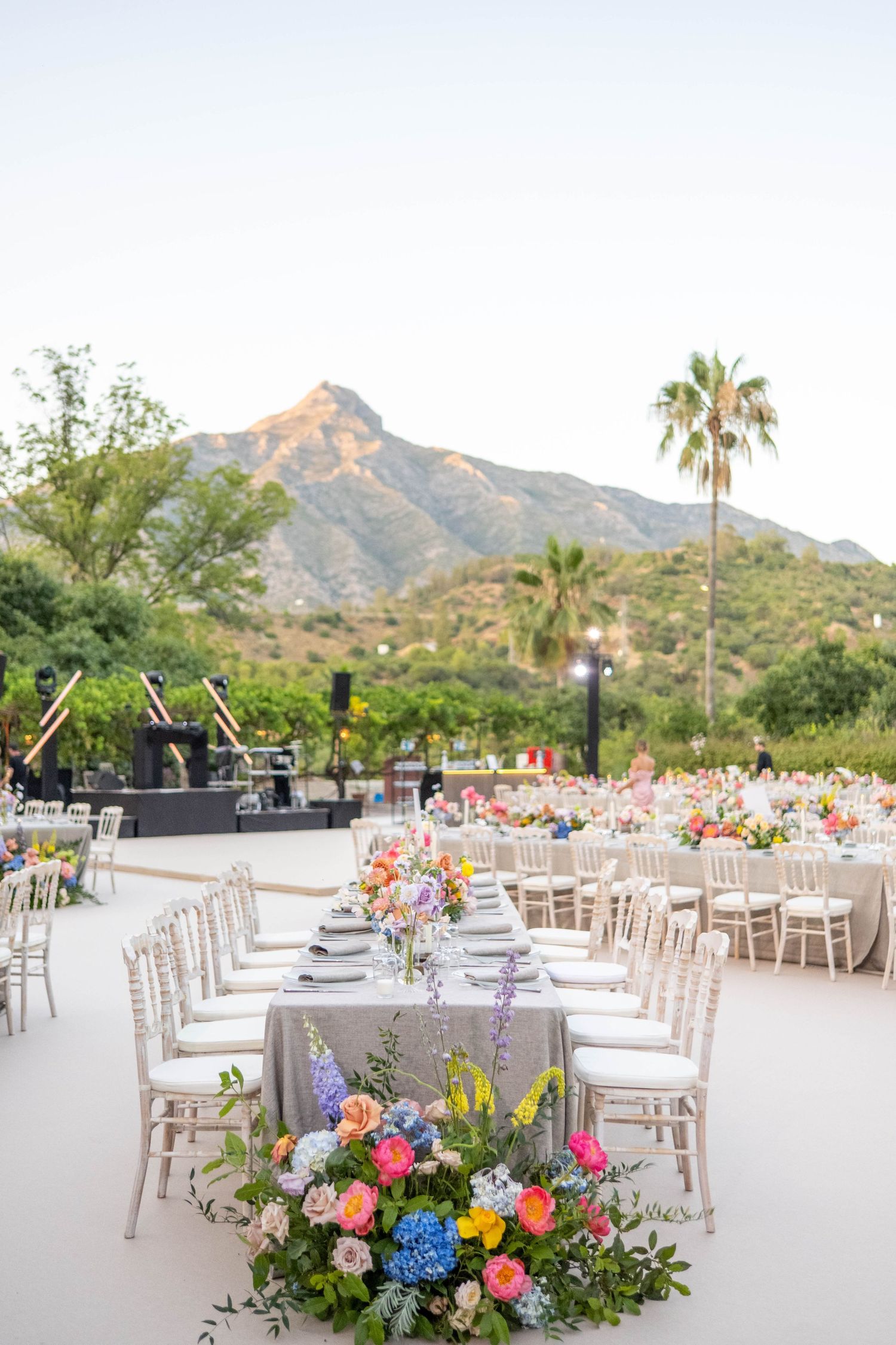 Elegant outdoor wedding reception tables with colorful floral centerpieces set against a mountain backdrop.