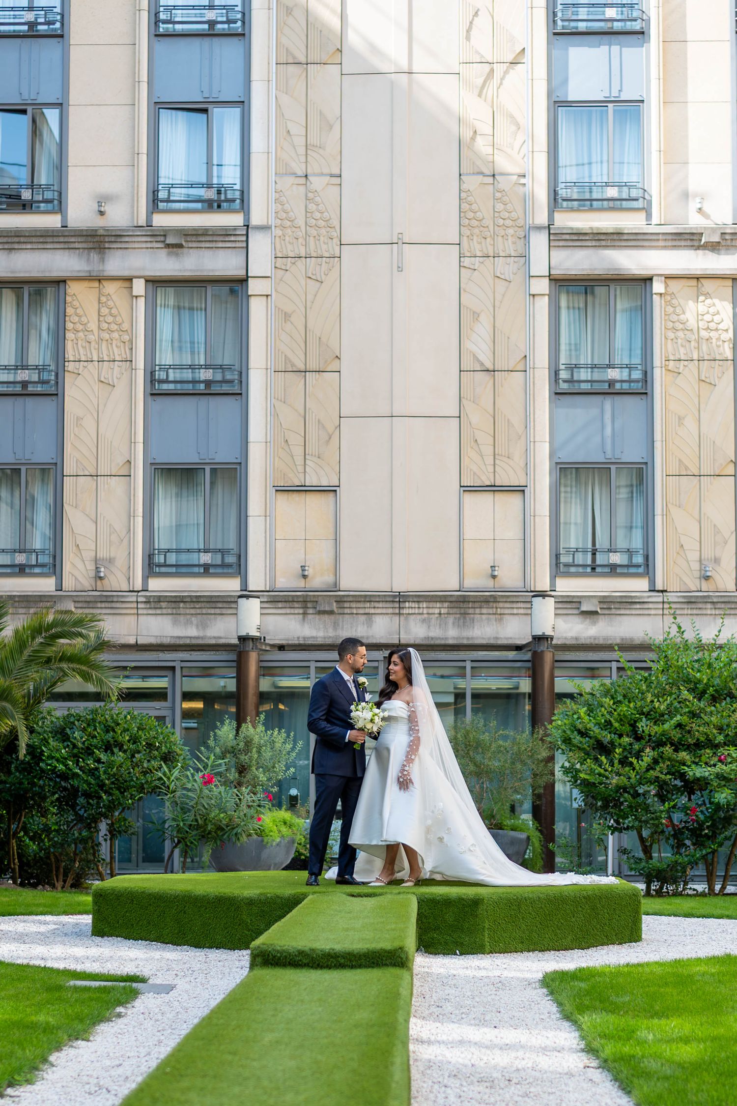 A wedding ceremony sequence on a manicured lawn with a white stone path leading to a modern building exterior.