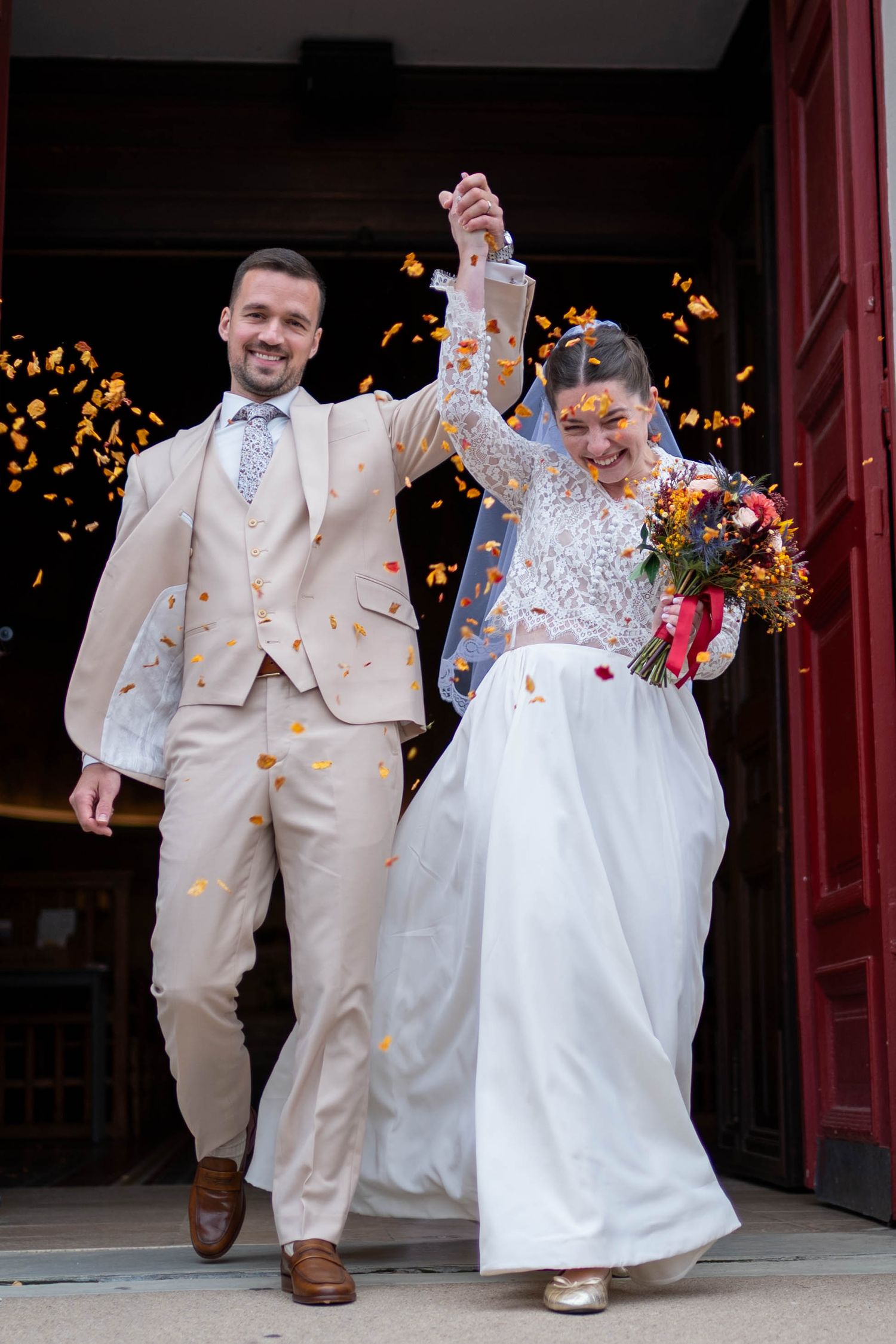 Newlyweds exit church doors while guests throw flower petals in celebration.