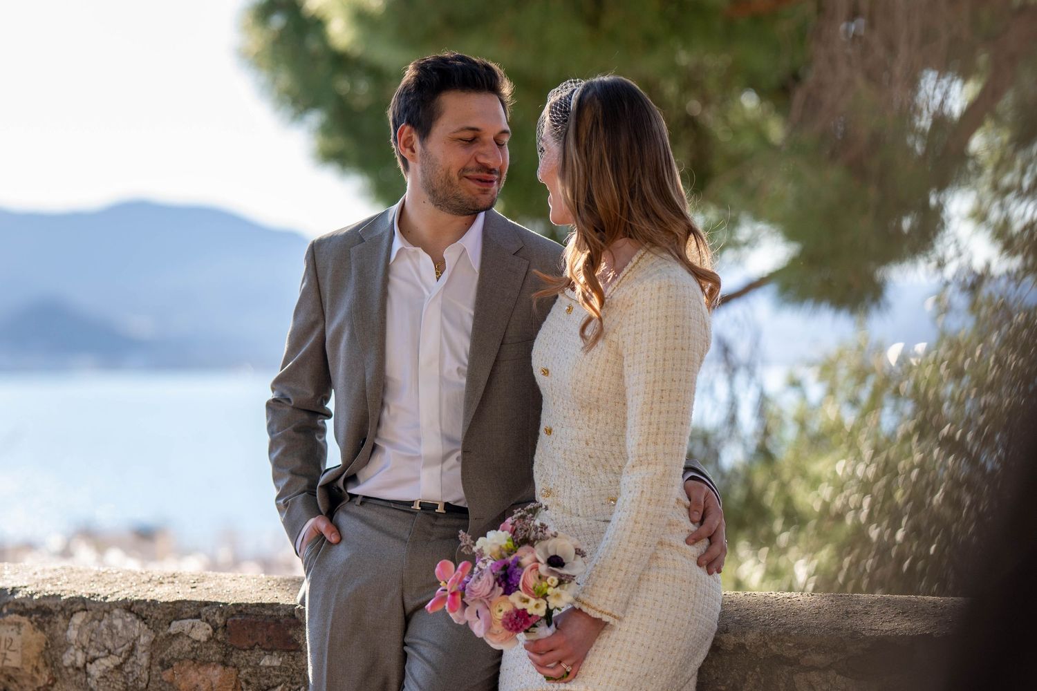 A couple in wedding attire embraces during a romantic outdoor photoshoot with mountain and ocean views.