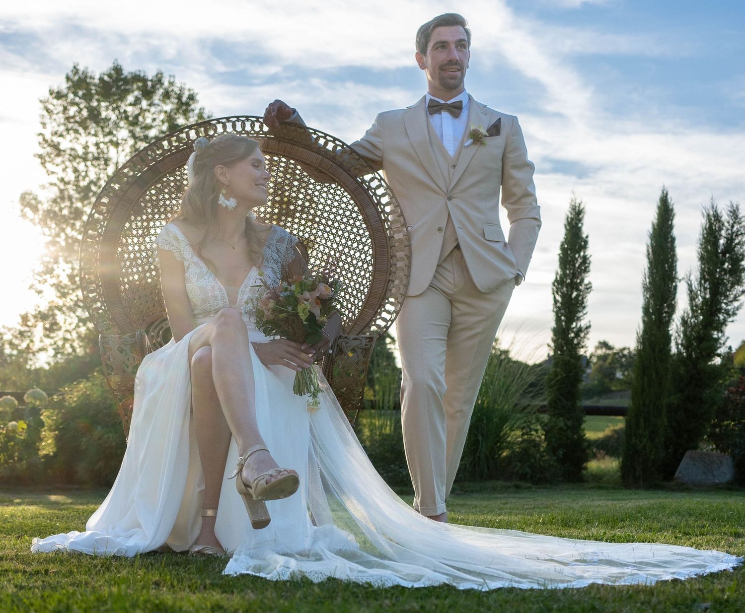 Wedding couple posing in golden sunlight with tall cypress trees in background.
