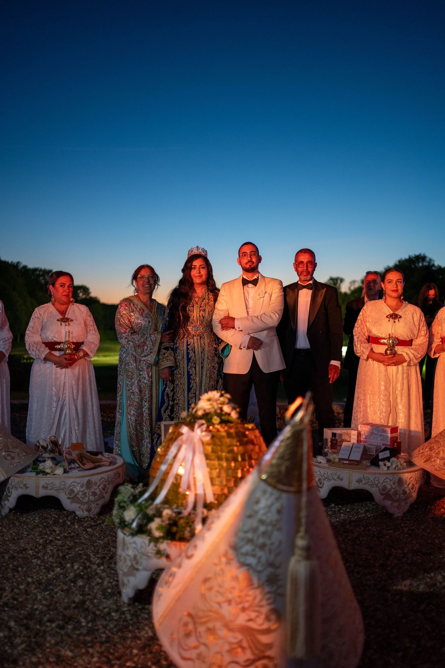 A group stands outdoors at dusk behind decorative wedding displays illuminated by warm lighting.