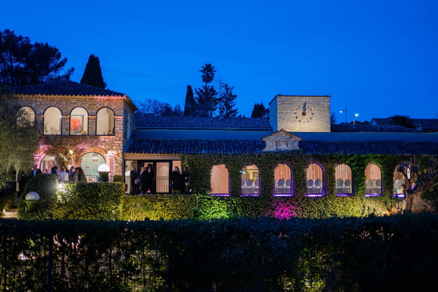 Historic stone building with arched windows illuminated at dusk against deep blue sky.