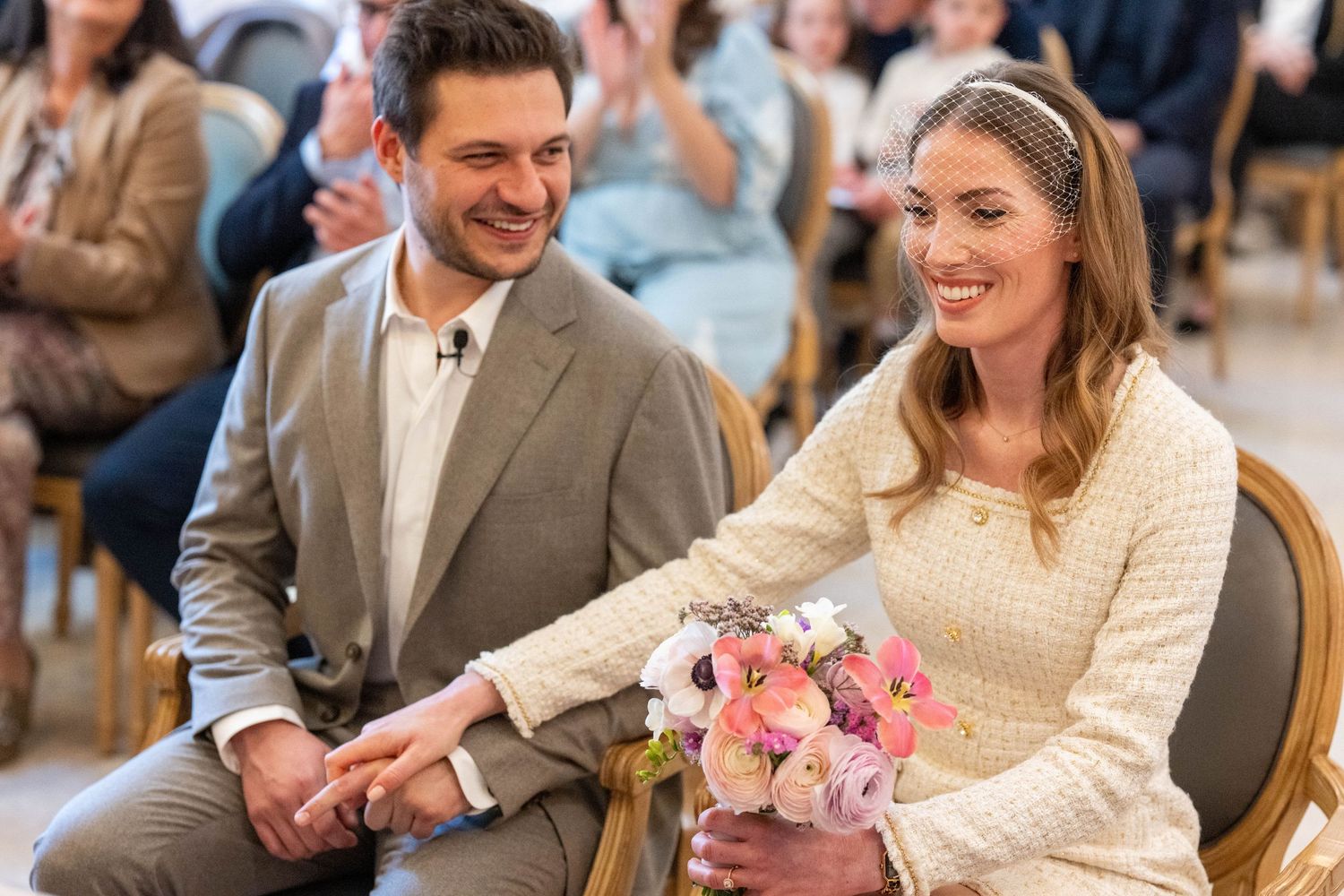 A couple shares a joyful moment at a wedding reception with pink floral centerpieces and guests in the background.