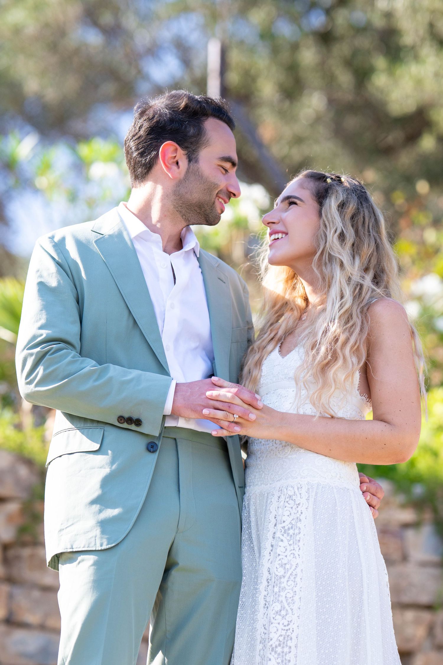 A couple shares joyful moments together outdoors, with one wearing a mint green suit and the other in white lace.