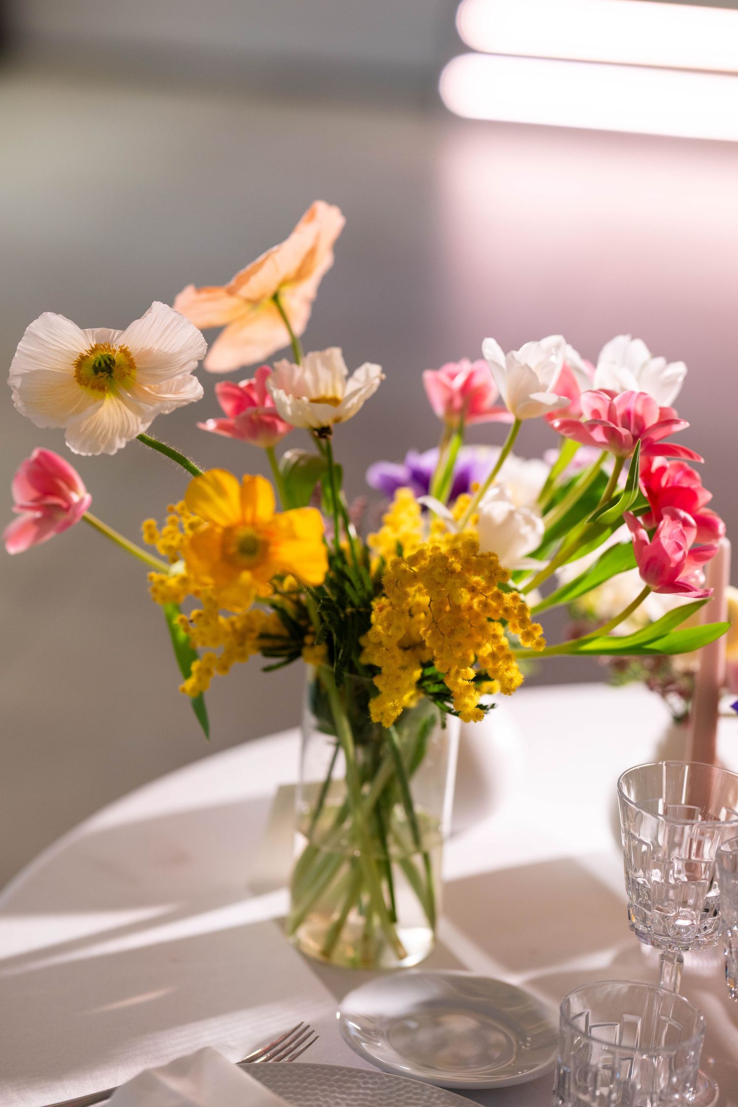Colorful spring flowers arranged in glass vases on a sunlit table with crystal glassware.