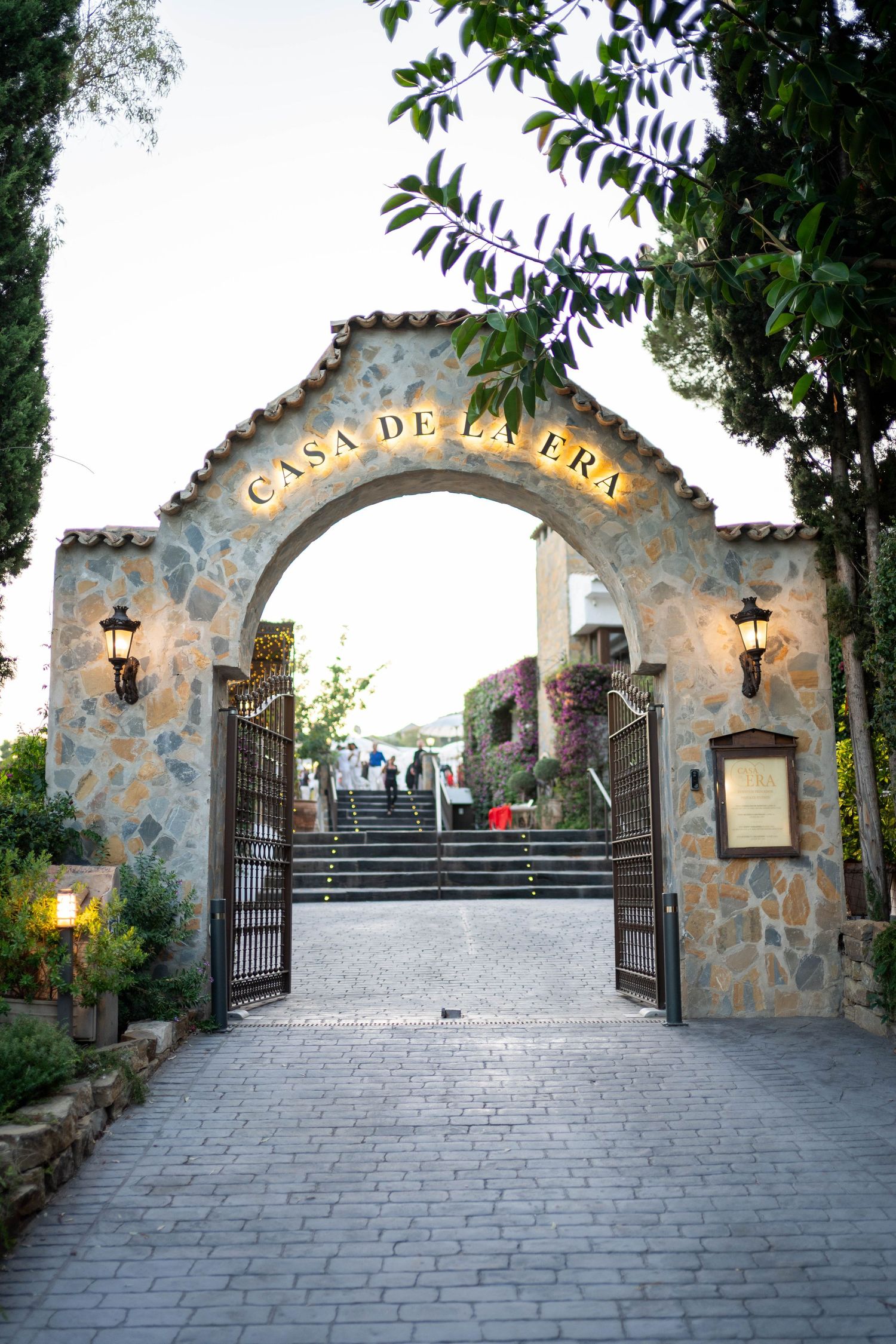 Stone archway entrance with 'Casa de la Era' sign and lanterns leading up stone steps.