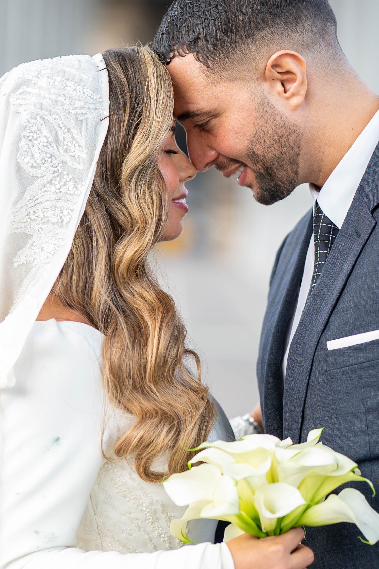 Newlywed couple shares an intimate moment while holding a bouquet of white calla lilies.