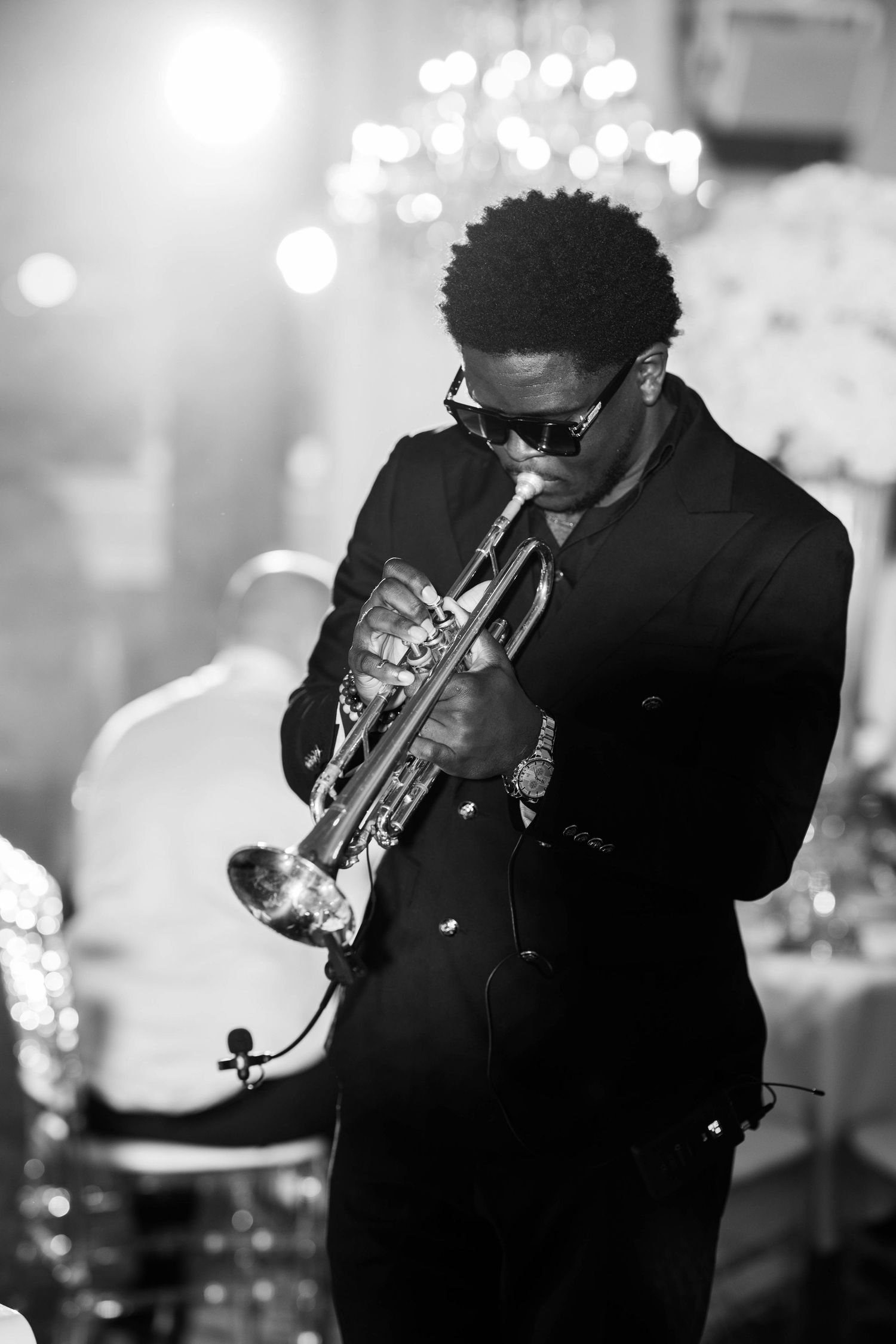 A jazz musician plays trumpet on stage in a dark venue with bokeh lights in the background.