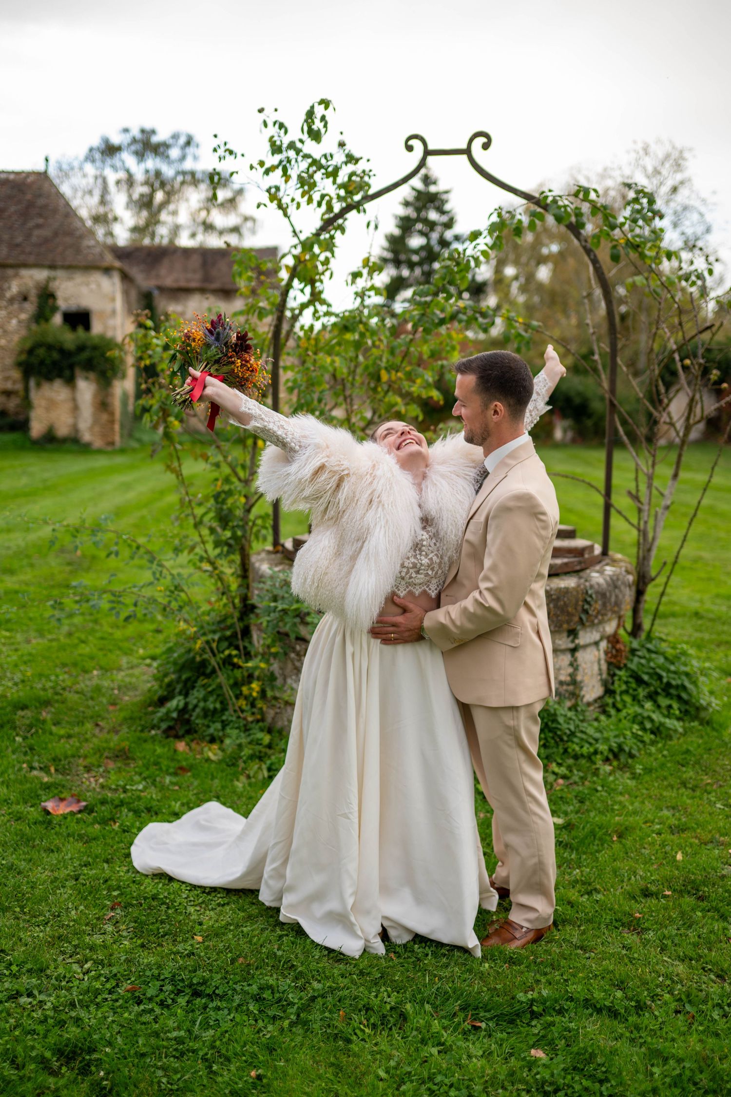 Wedding couple in white dress and beige suit dancing playfully in a garden setting.