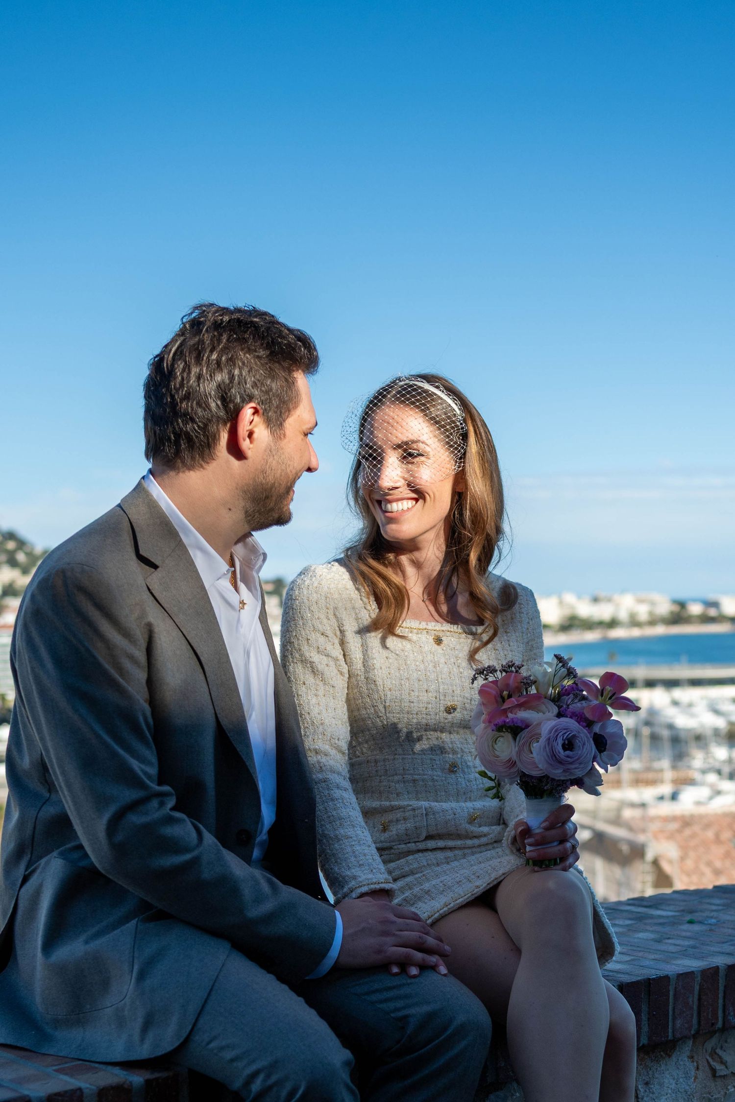 A couple shares a romantic moment overlooking a coastal town on a bright sunny day.