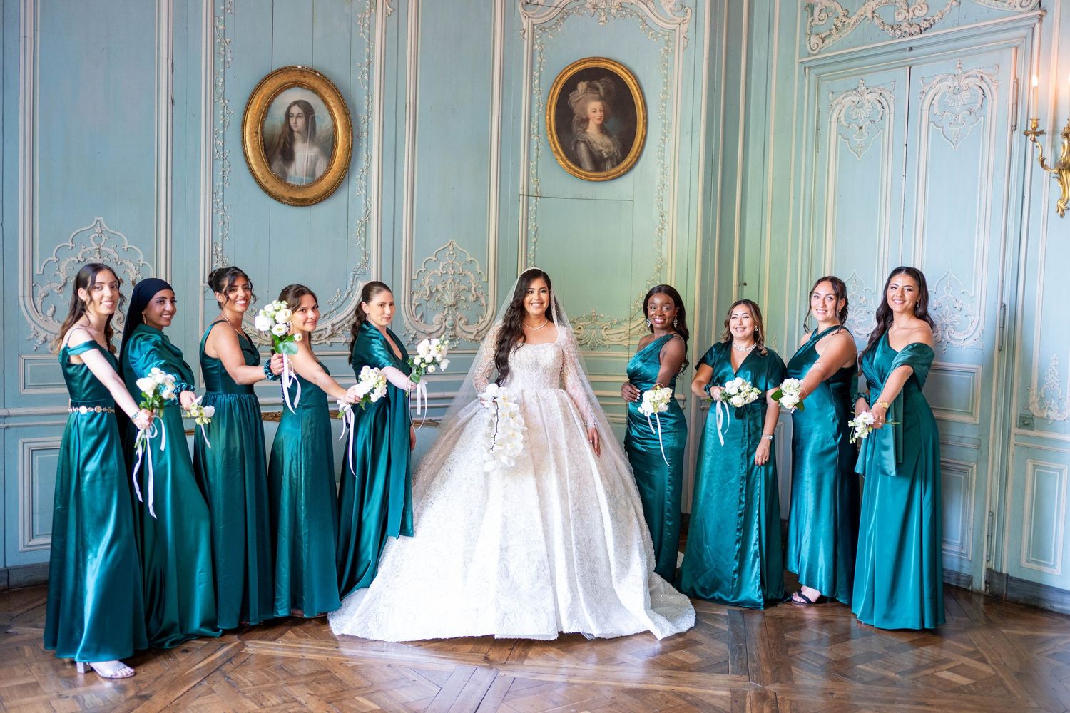 Wedding party poses in an elegant blue-walled room with ornate gold trim and portraits.