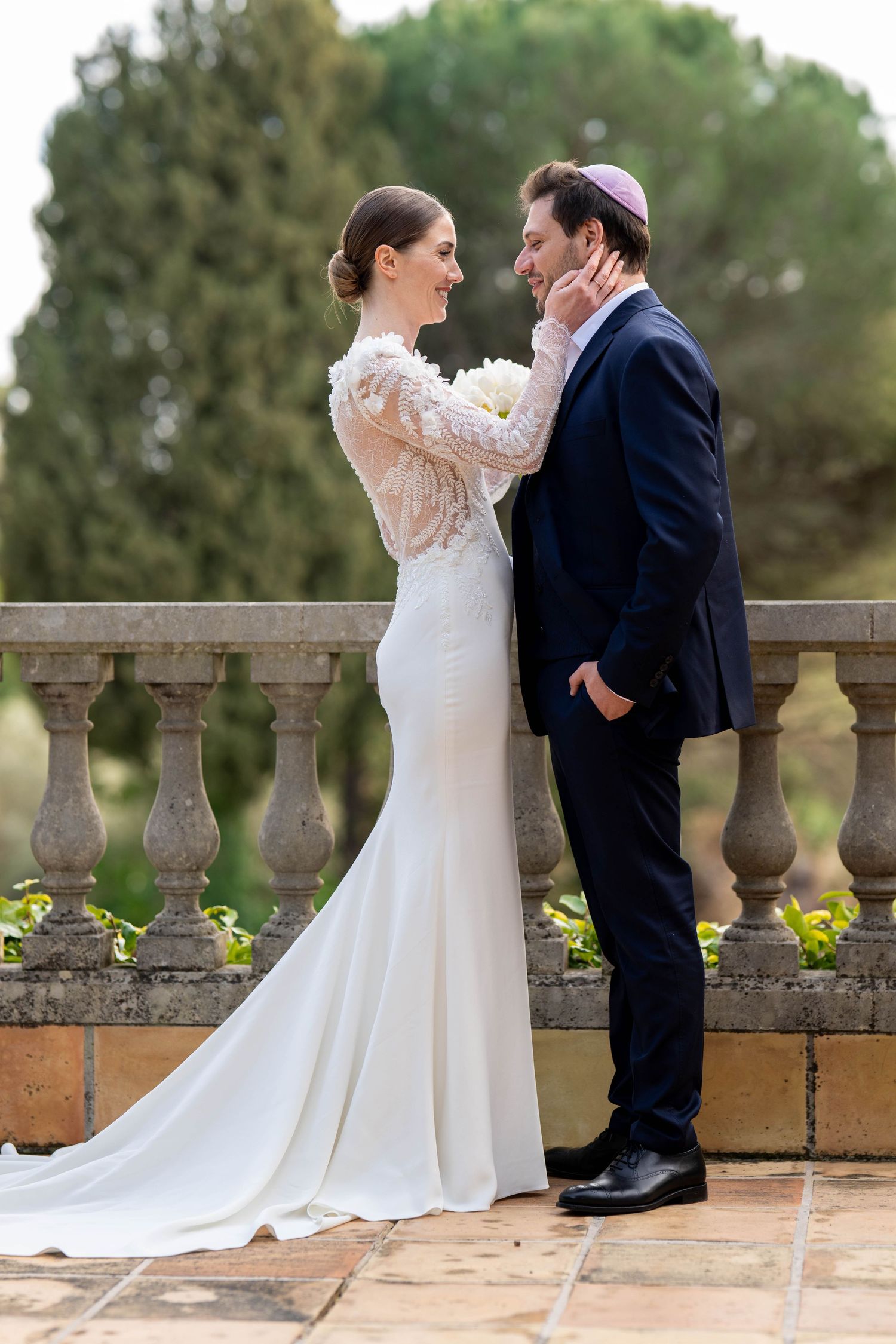 Elegant wedding couple posing by stone balustrade in formal garden setting.