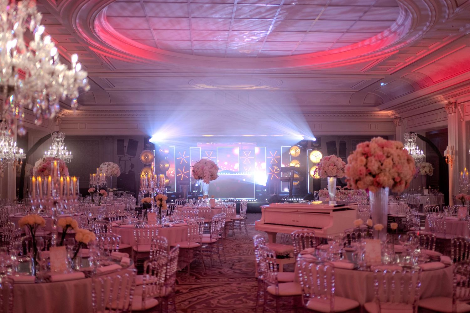 Luxurious wedding reception ballroom with dramatic pink lighting and crystal chandeliers.