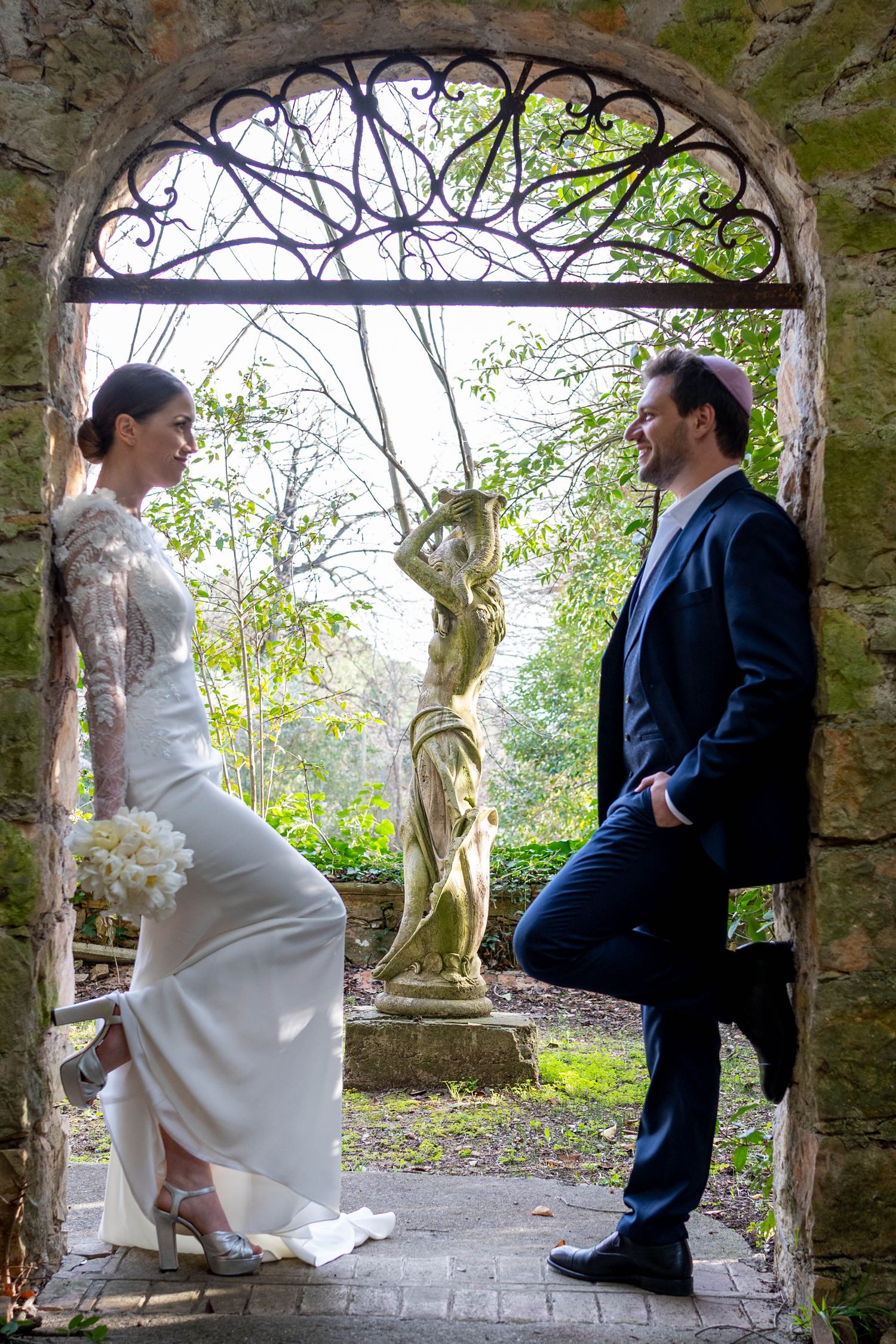 A couple in wedding attire shares romantic moments in a garden archway setting during a photo session.