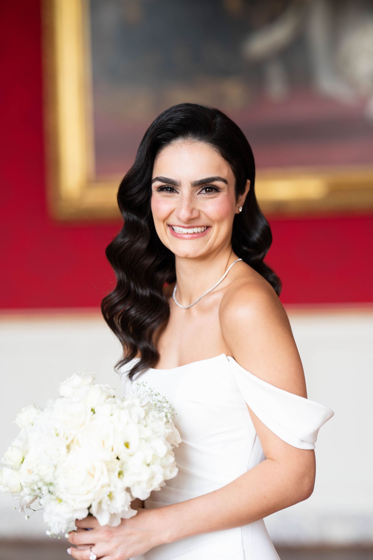 A bridal portrait series showing a woman in a white dress holding a bouquet of white flowers against a red wall background.