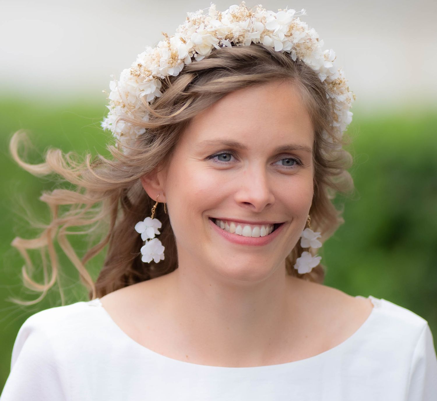 A bride wearing a delicate floral crown and pearl earrings smiles while her hair blows in the wind.