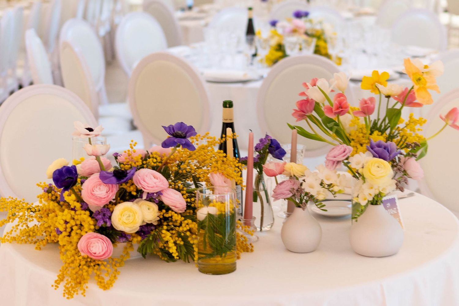 Colorful spring flower arrangements on white wedding reception tables.
