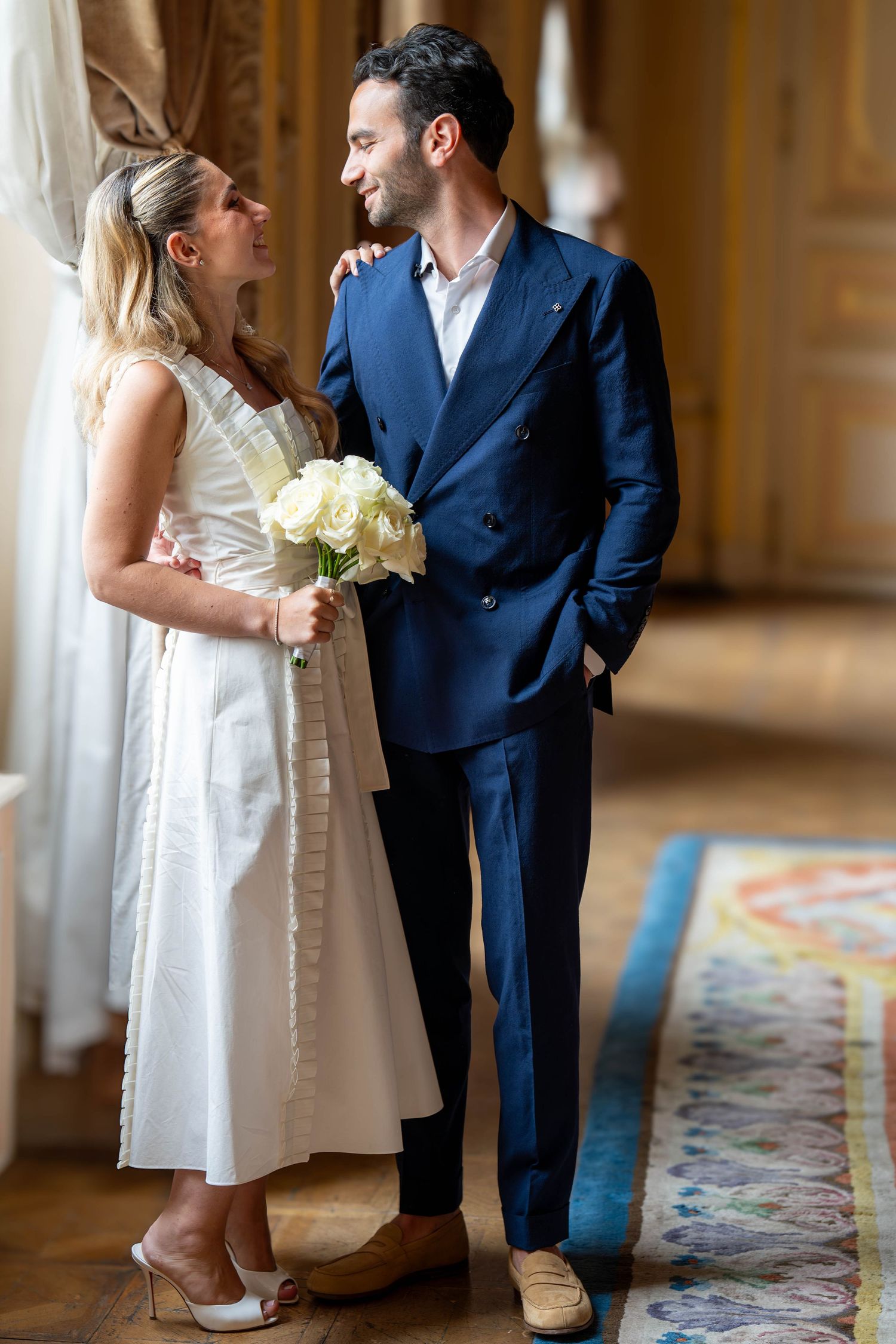 A couple in wedding attire shares intimate moments on a patterned carpet in an elegant indoor setting.