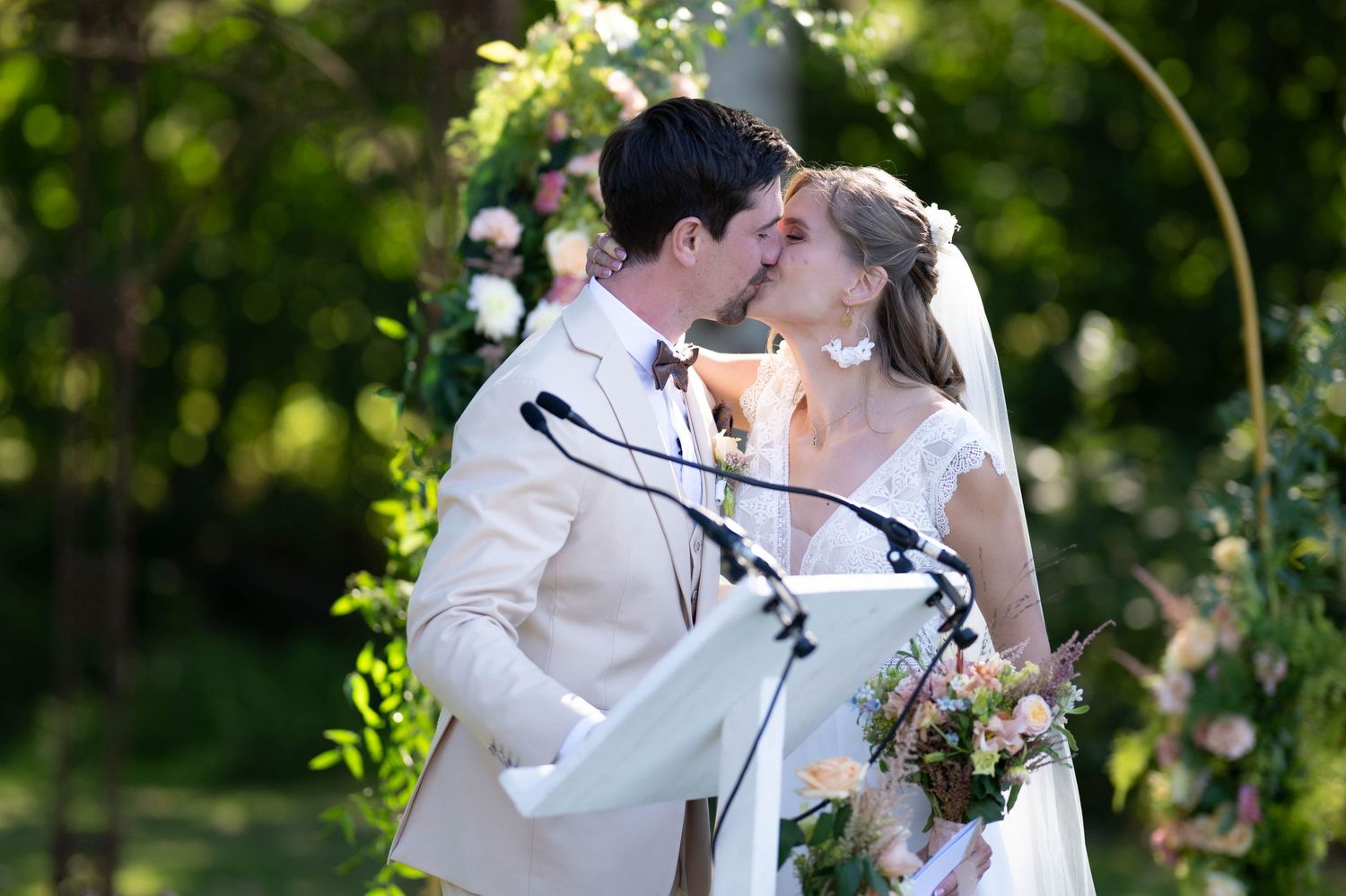 Romantic couple embraces in a lush garden setting with white floral decorations and natural greenery.