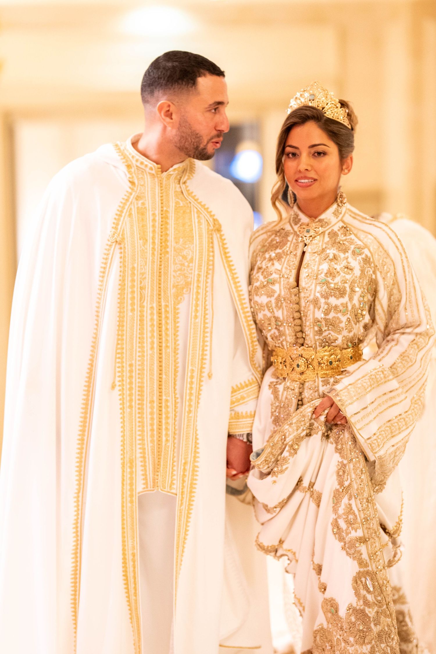 Wedding couple in traditional gold and white Moroccan wedding attire pose together.