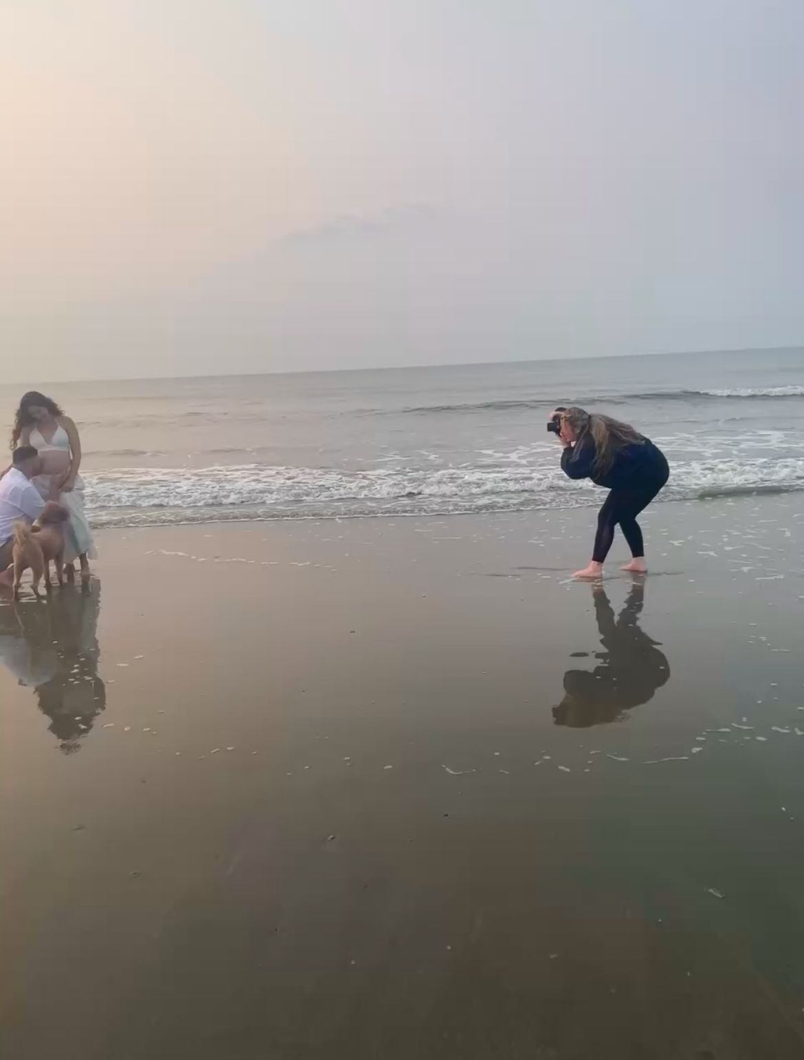 Taylor, owner of Raley & Roots photography taking photos on a misty beach at the ocean's edge with reflections in the wet sand.