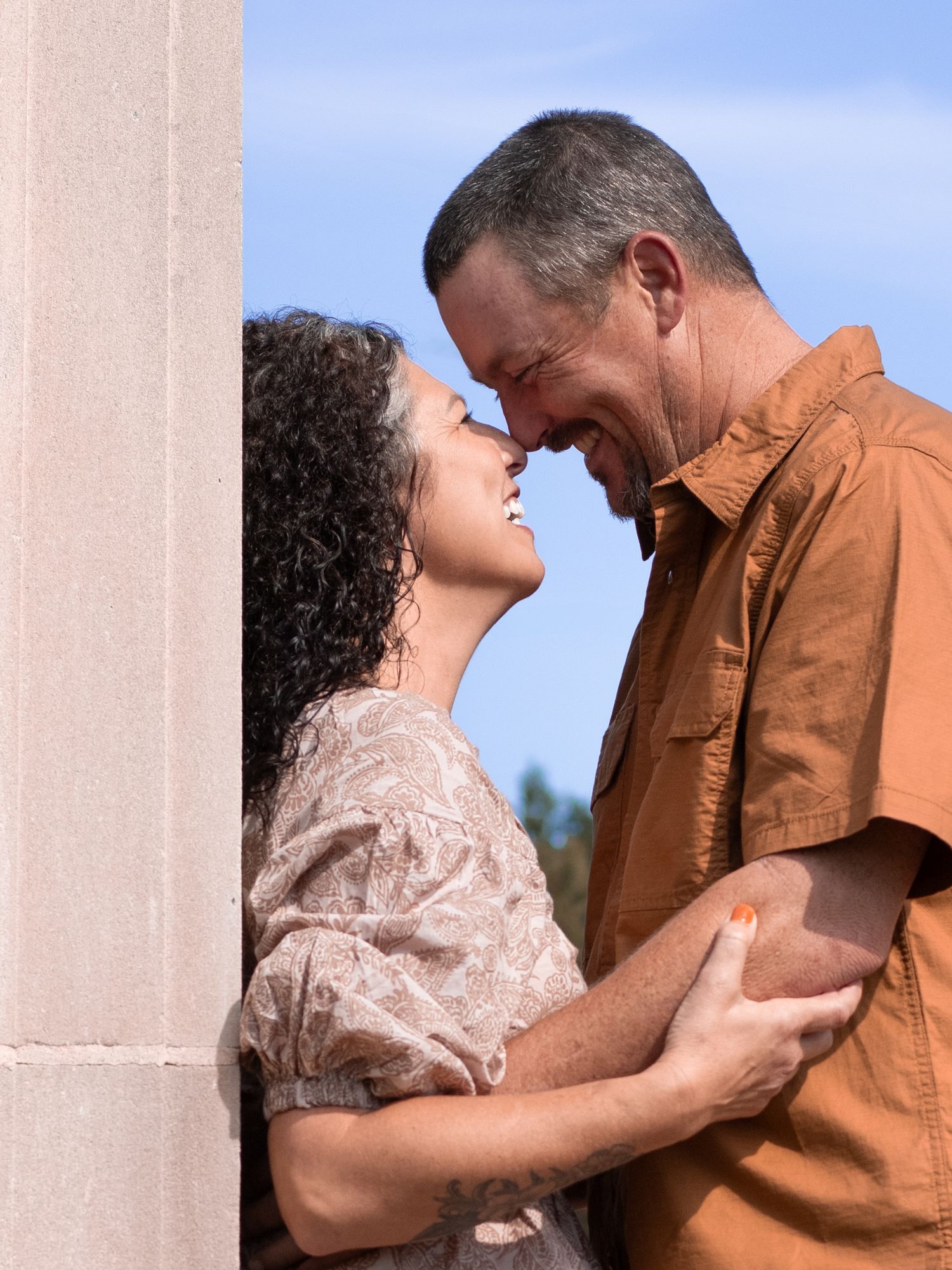 A romantic couple shares an intimate moment while embracing against a wall outdoors.