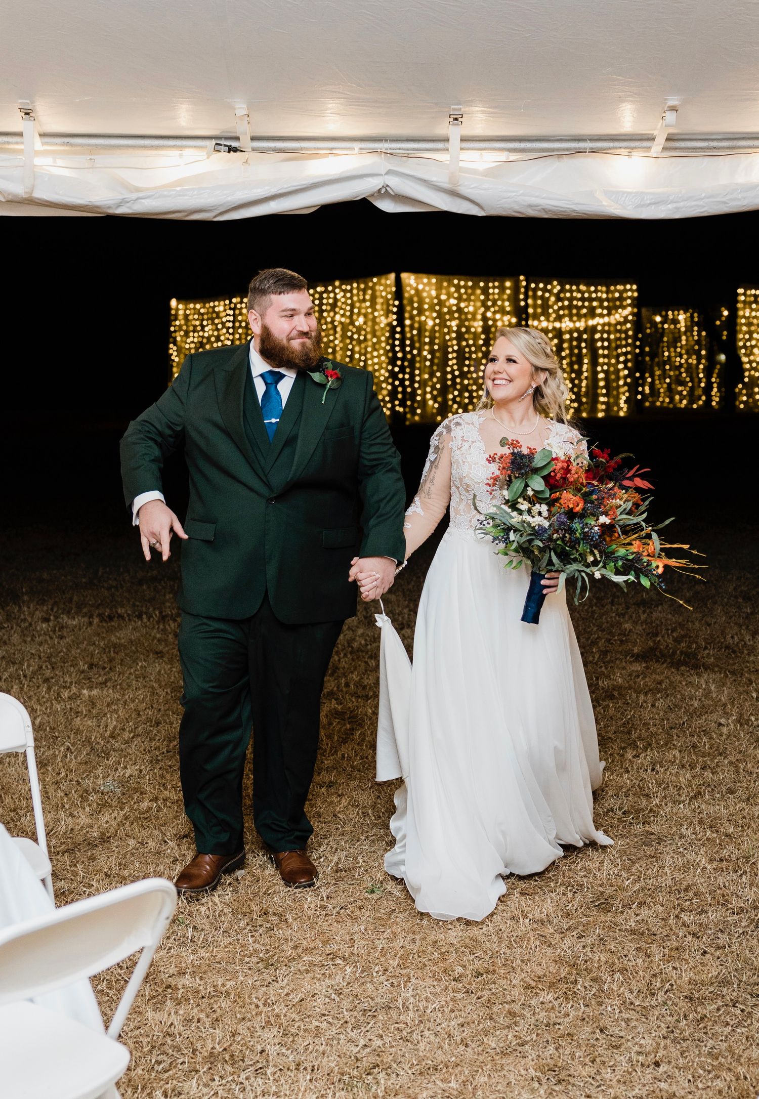 A wedding couple poses in front of a twinkling light backdrop while the groom gestures expressively during their reception.