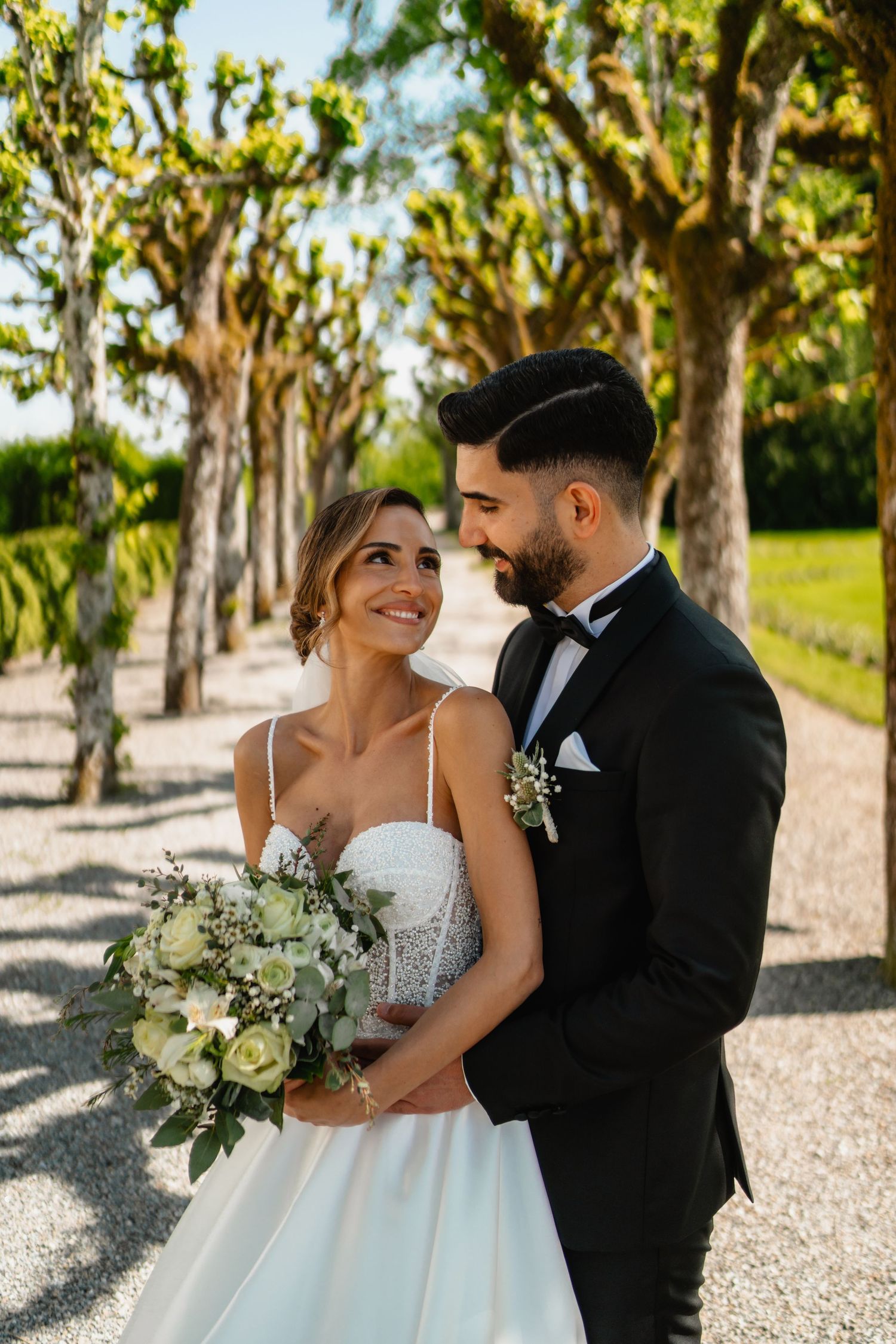 A romantic wedding photo session in a tree-lined pathway with natural sunlight filtering through.