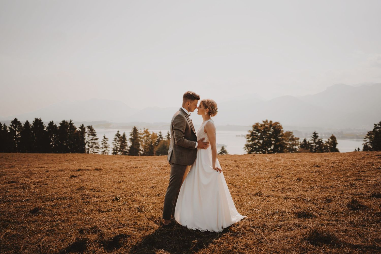 Wedding couple standing in a scenic mountain field at golden hour.