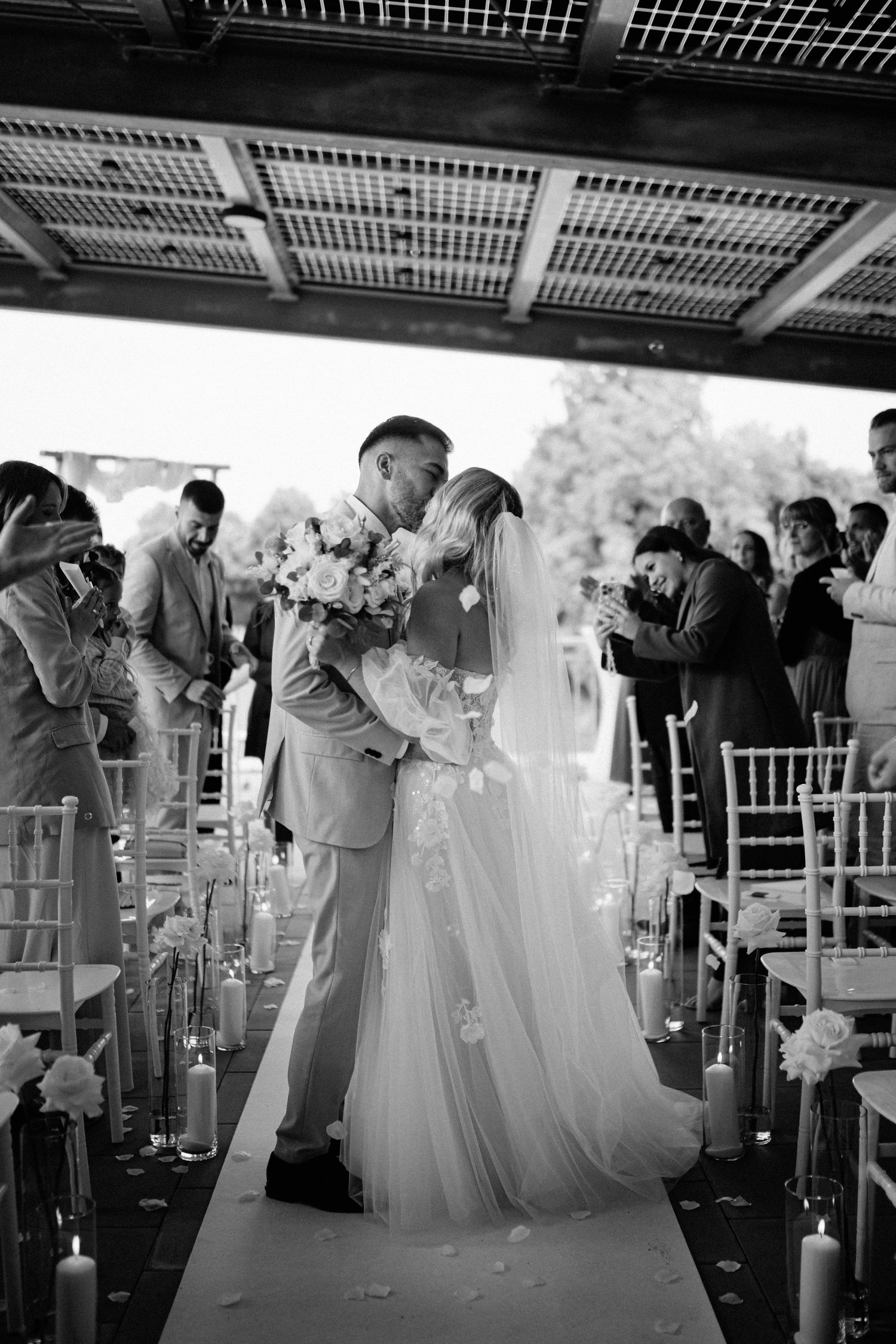 Wedding ceremony guests stand and celebrate during an emotional moment under a covered outdoor venue.