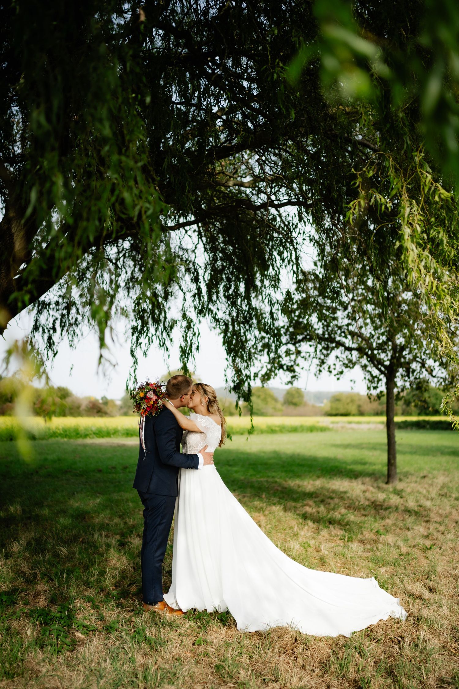 A couple shares a romantic moment under a weeping willow tree on their wedding day.