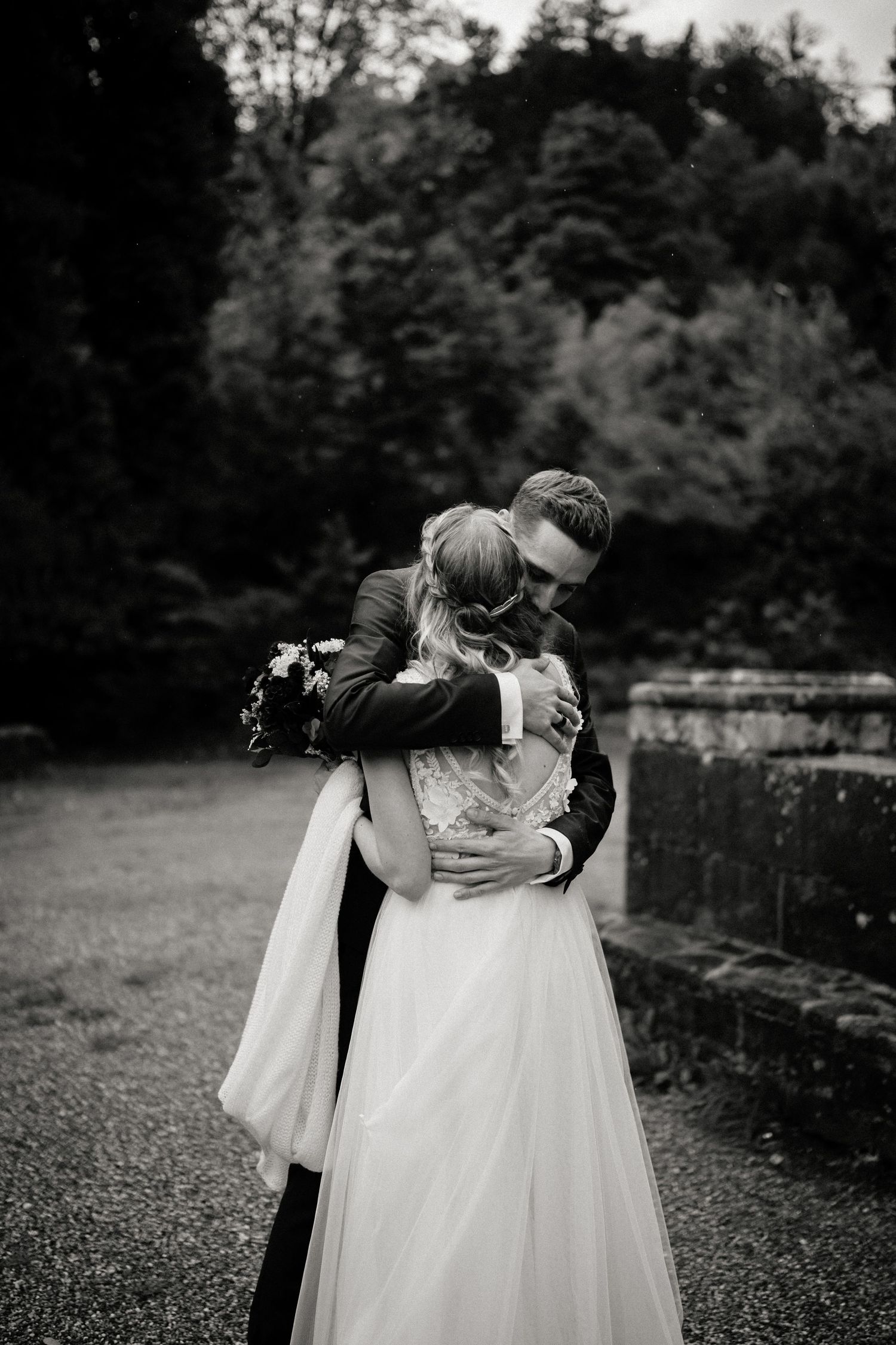 Black and white photo of couple embracing in intimate moment on gravel path.