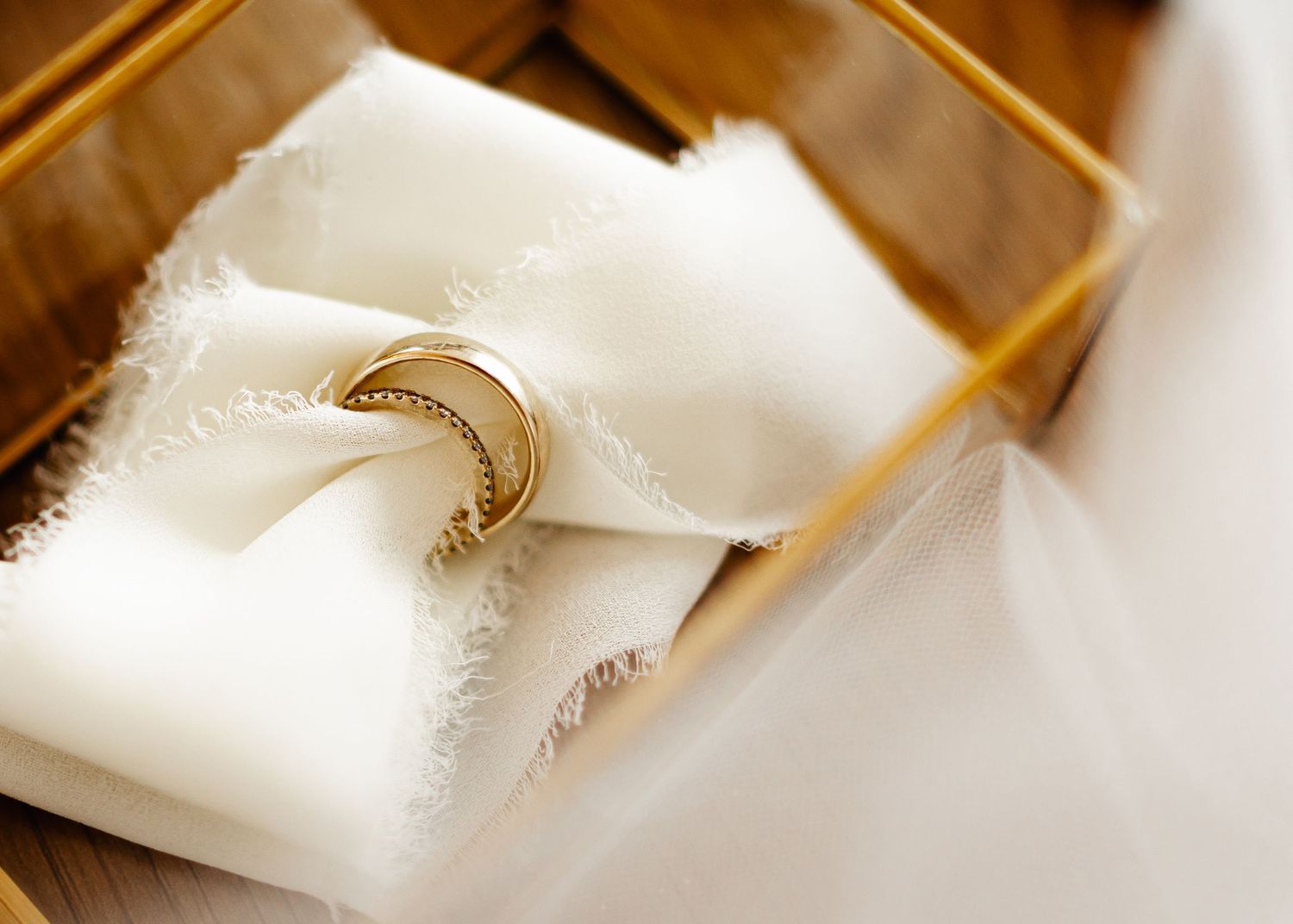 Close-up of wedding rings on white fabric with warm golden lighting.