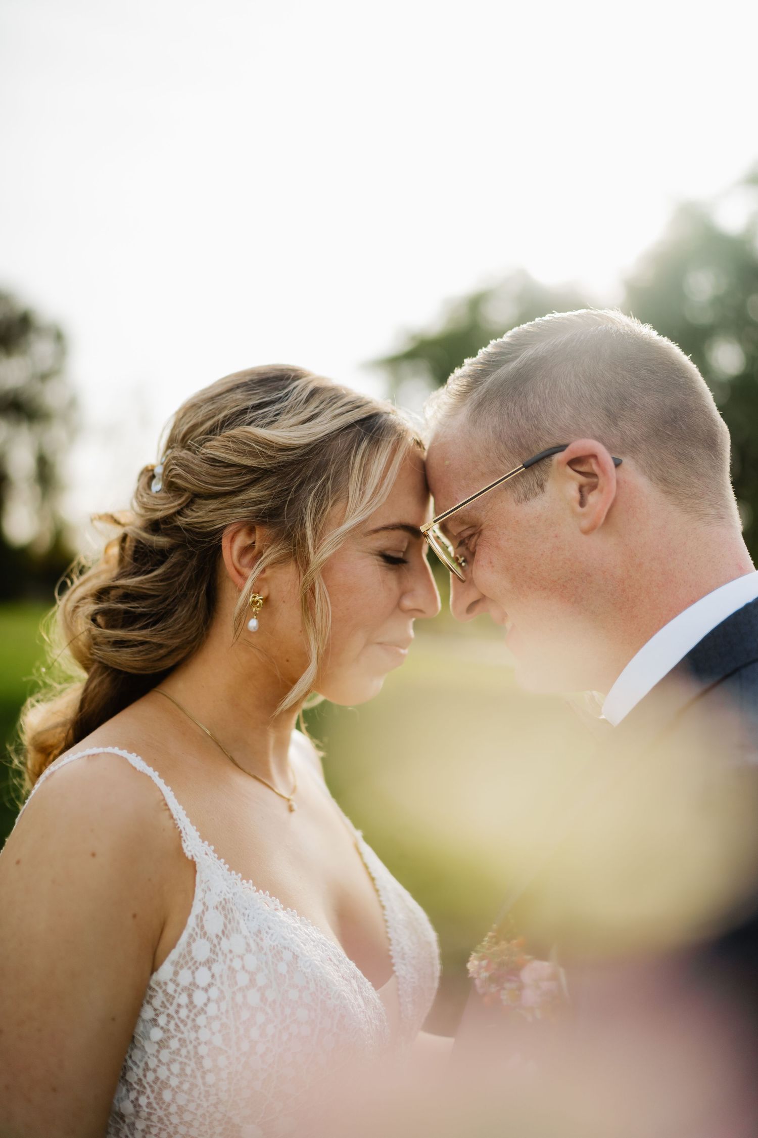A wedding couple shares an intimate kiss on their special day while being backlit by golden sunlight.