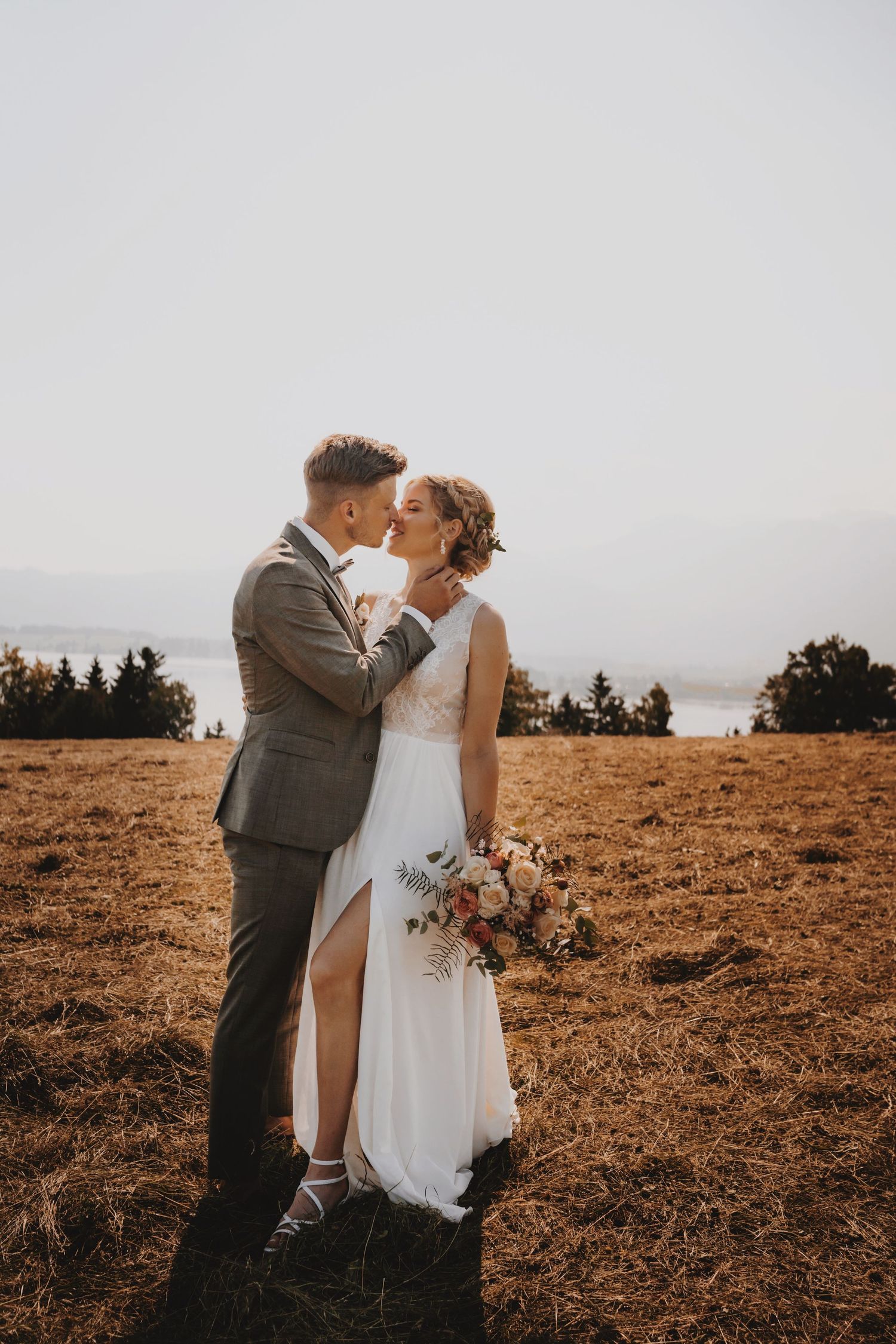 Sunset wedding portrait on a golden hillside with mountain silhouettes in the distance.