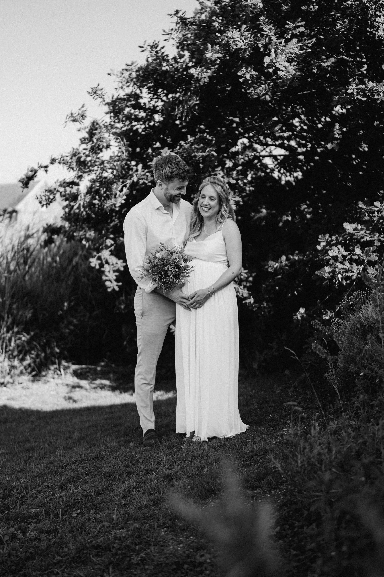 Black and white portrait of a couple standing together on a grassy hillside.