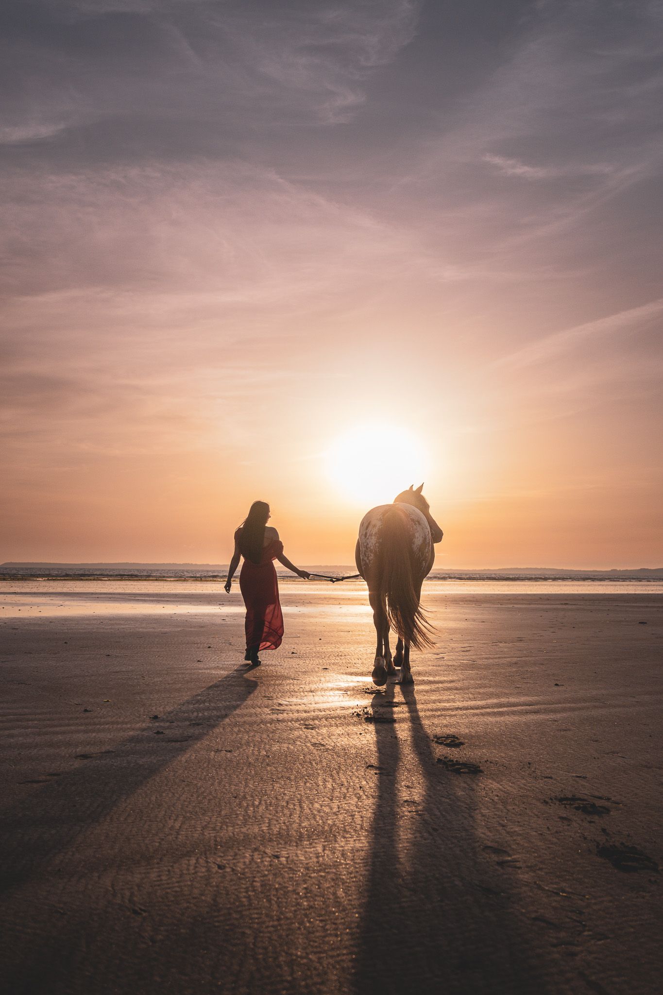 Femme en robe rouge marchant avec un cheval sur la plage au coucher de soleil – photographe Bretagne