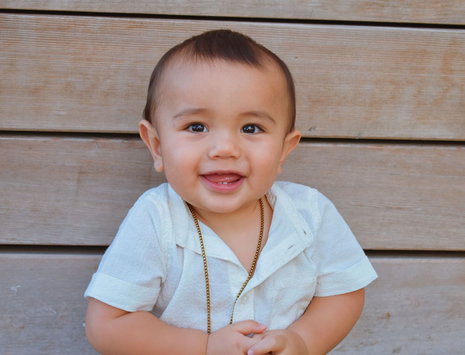 Baby in white shirt smiling while sitting on wooden deck.