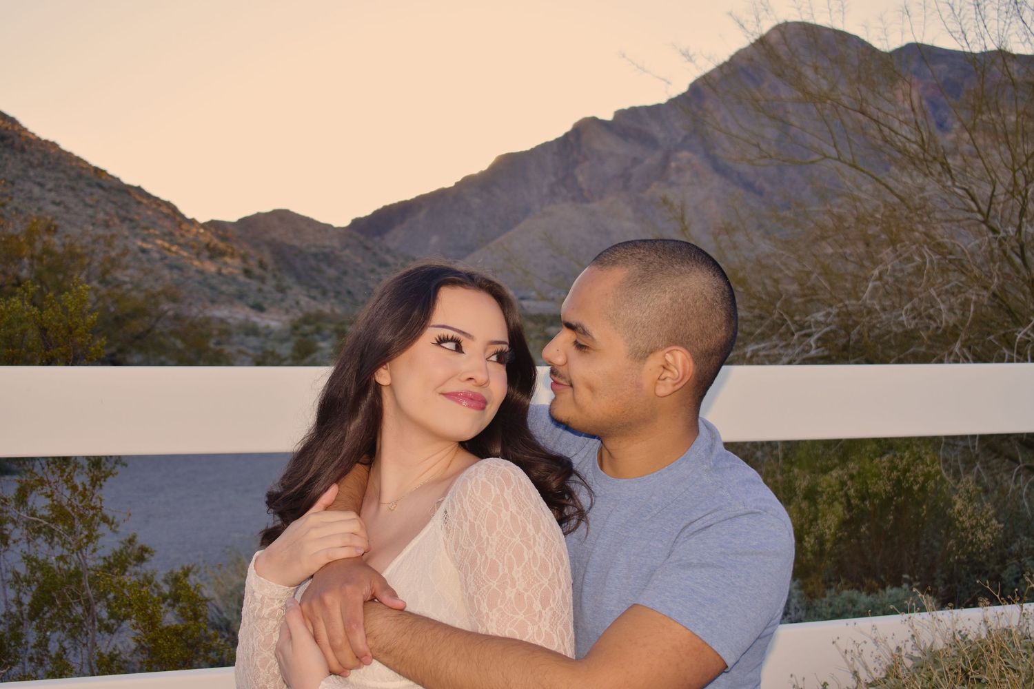 A couple embraces during sunset in a desert mountain landscape with warm golden lighting.