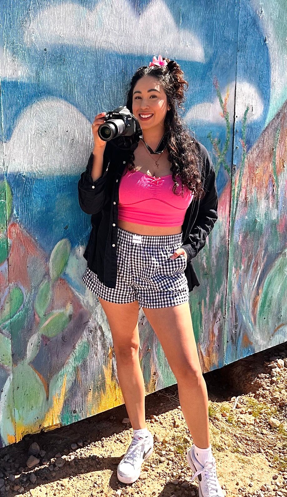 Woman in pink crop top and gingham shorts poses playfully against colorful graffiti wall in multiple shots.