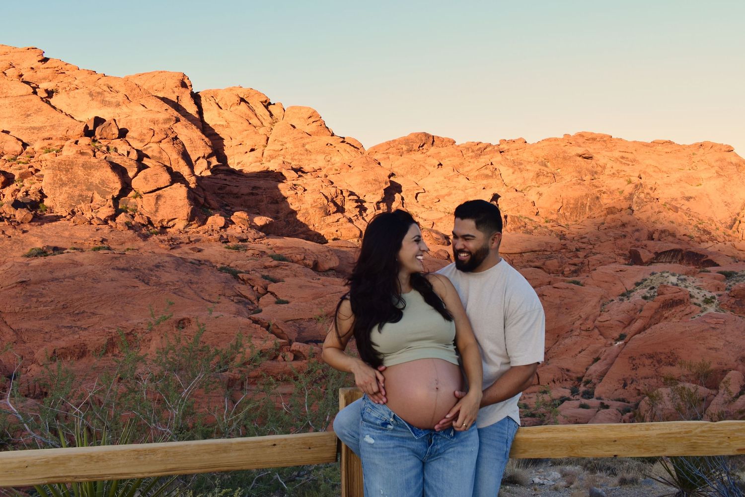 A maternity photoshoot with dramatic red rock formations in the background during golden hour.