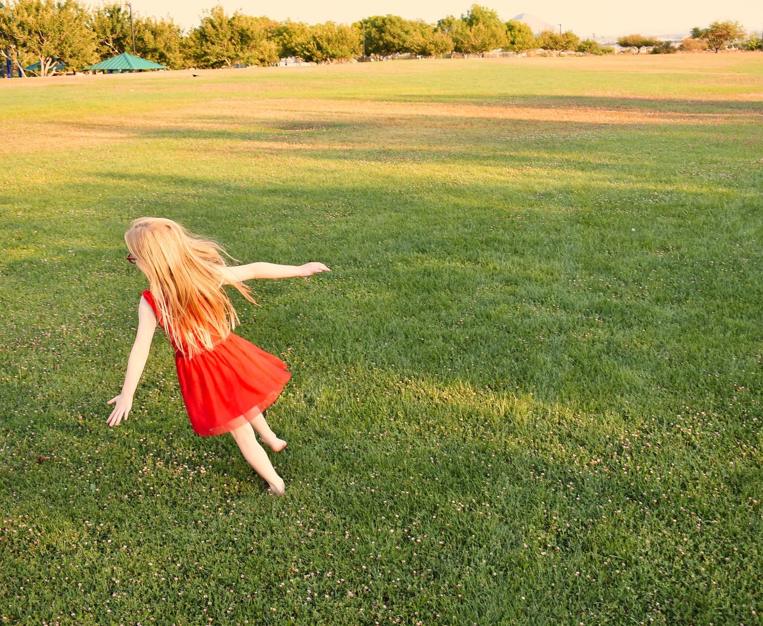 People playing and running in a green field during golden hour.