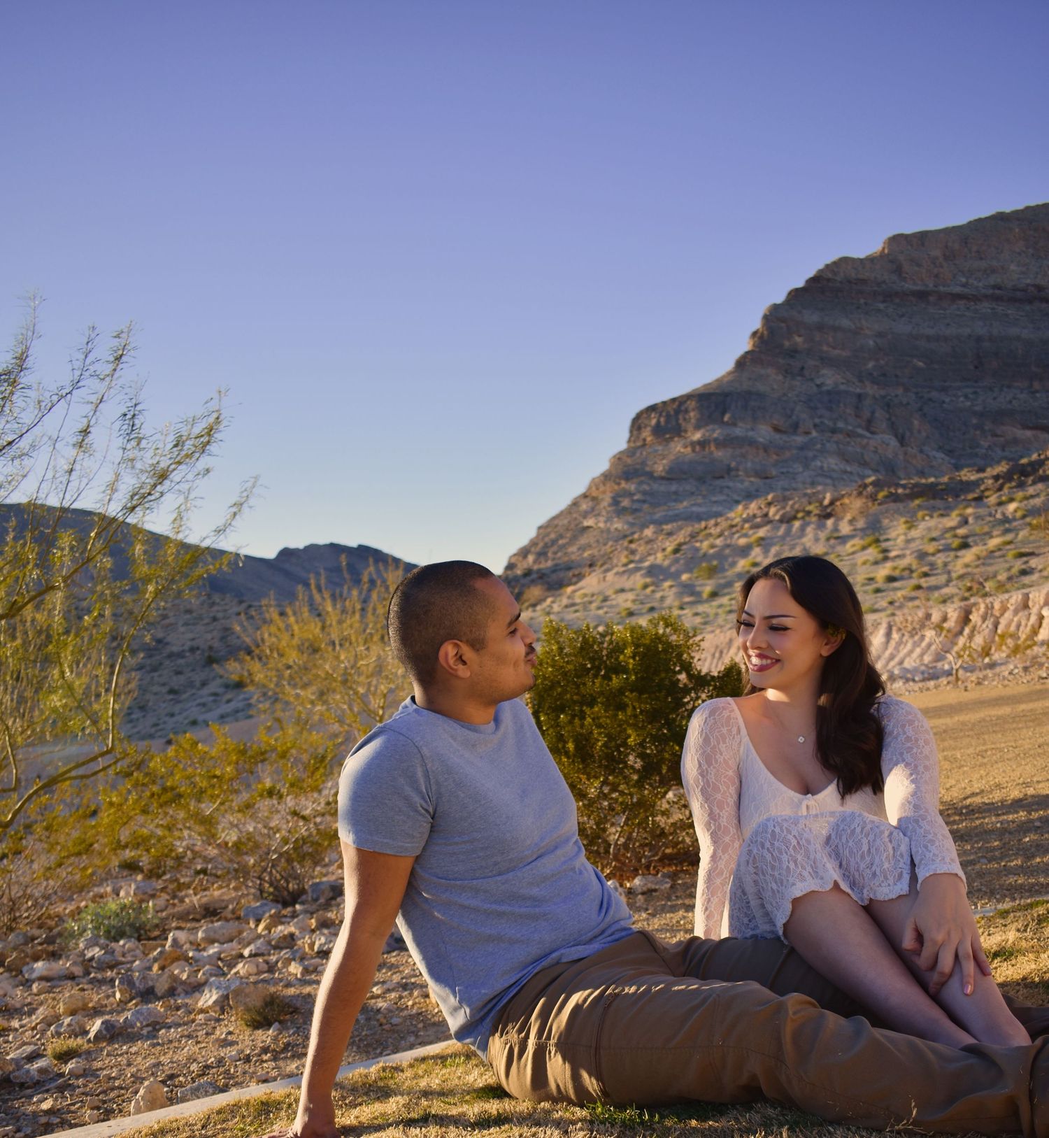 Couple relaxing on desert rocks with scenic mountain backdrop during golden hour in natural landscape.