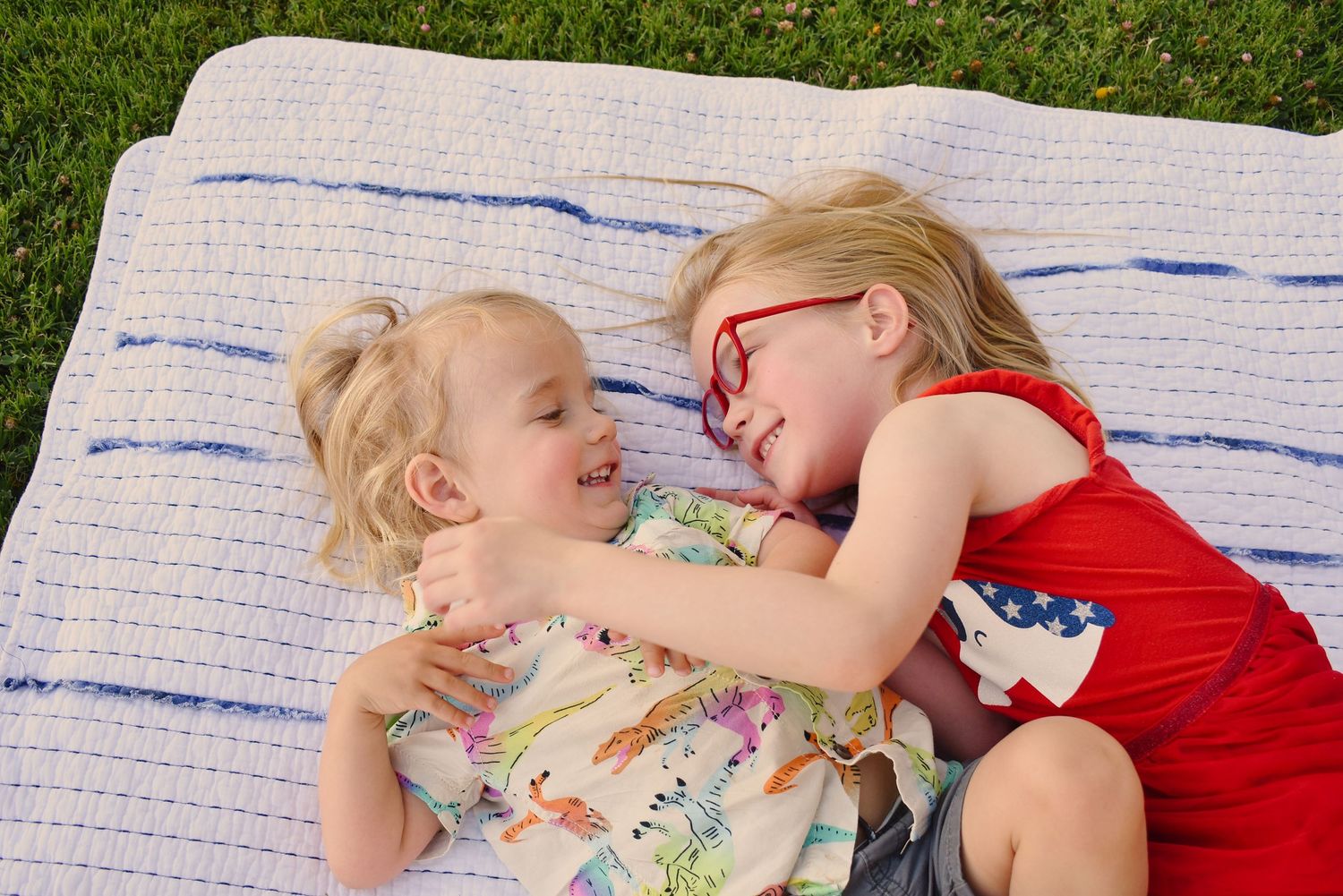 Children laying on a striped blanket and playing together outdoors.