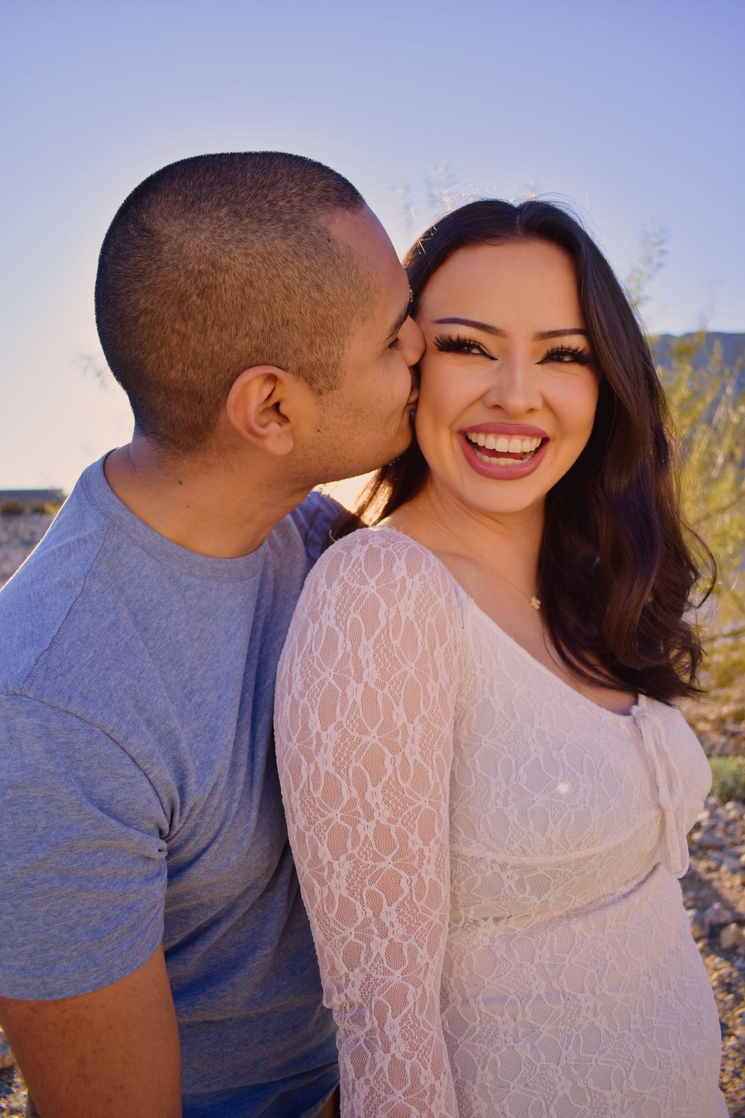 A couple embraces outdoors during a romantic photoshoot with desert scenery in the background.