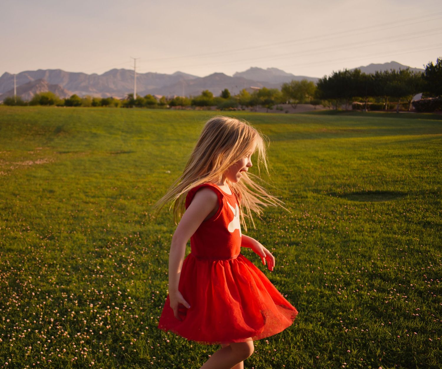 A sequence of twirling movements in a red dress against mountain scenery at sunset.