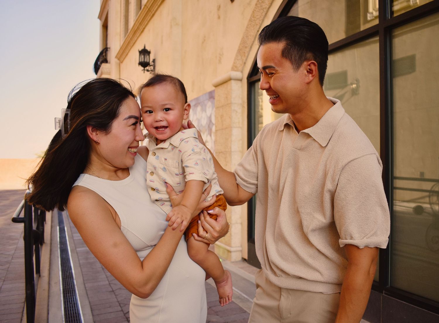 A family of three shares joyful moments together against a beige wall.