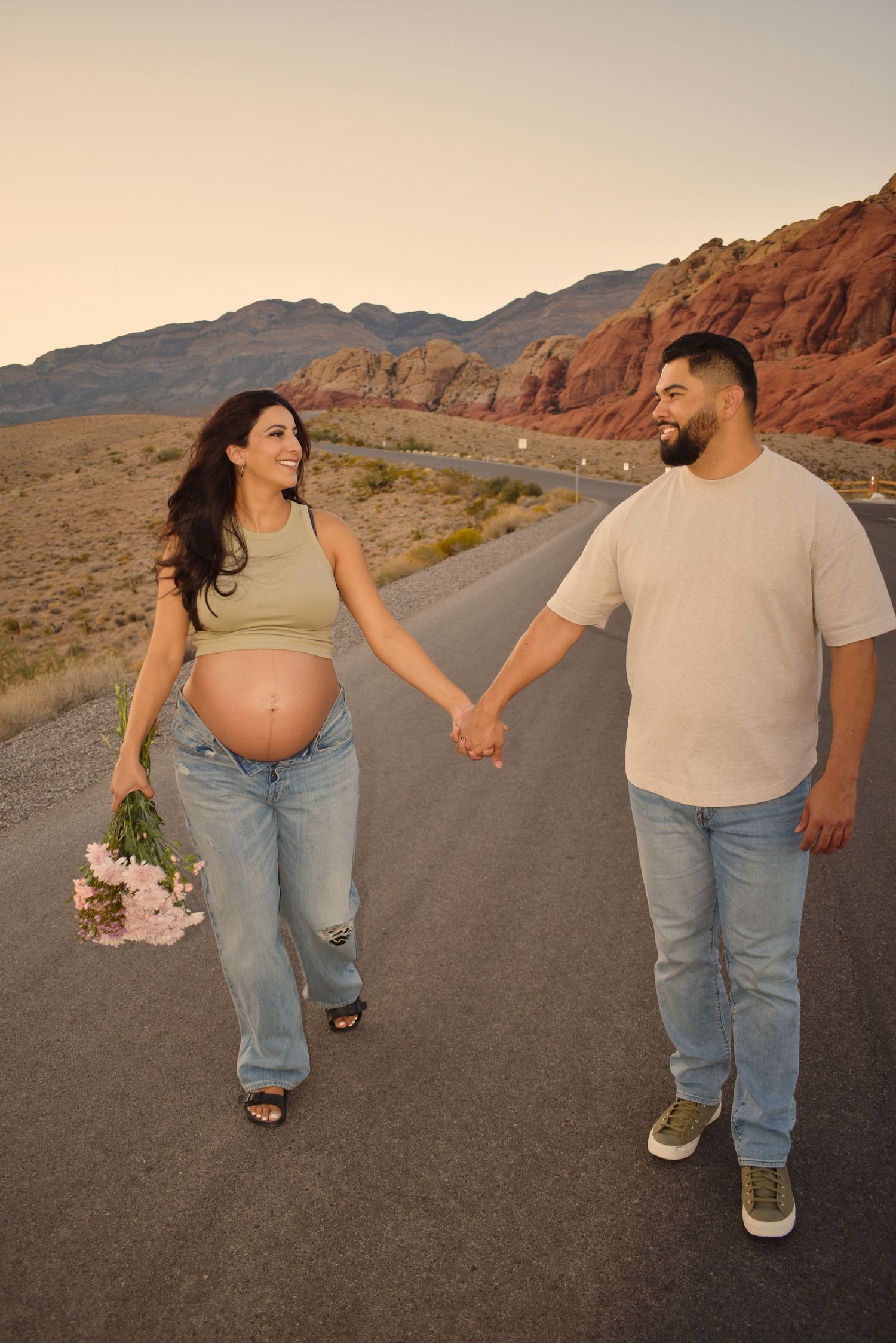 A couple strolls together on an empty road through dramatic desert landscape.